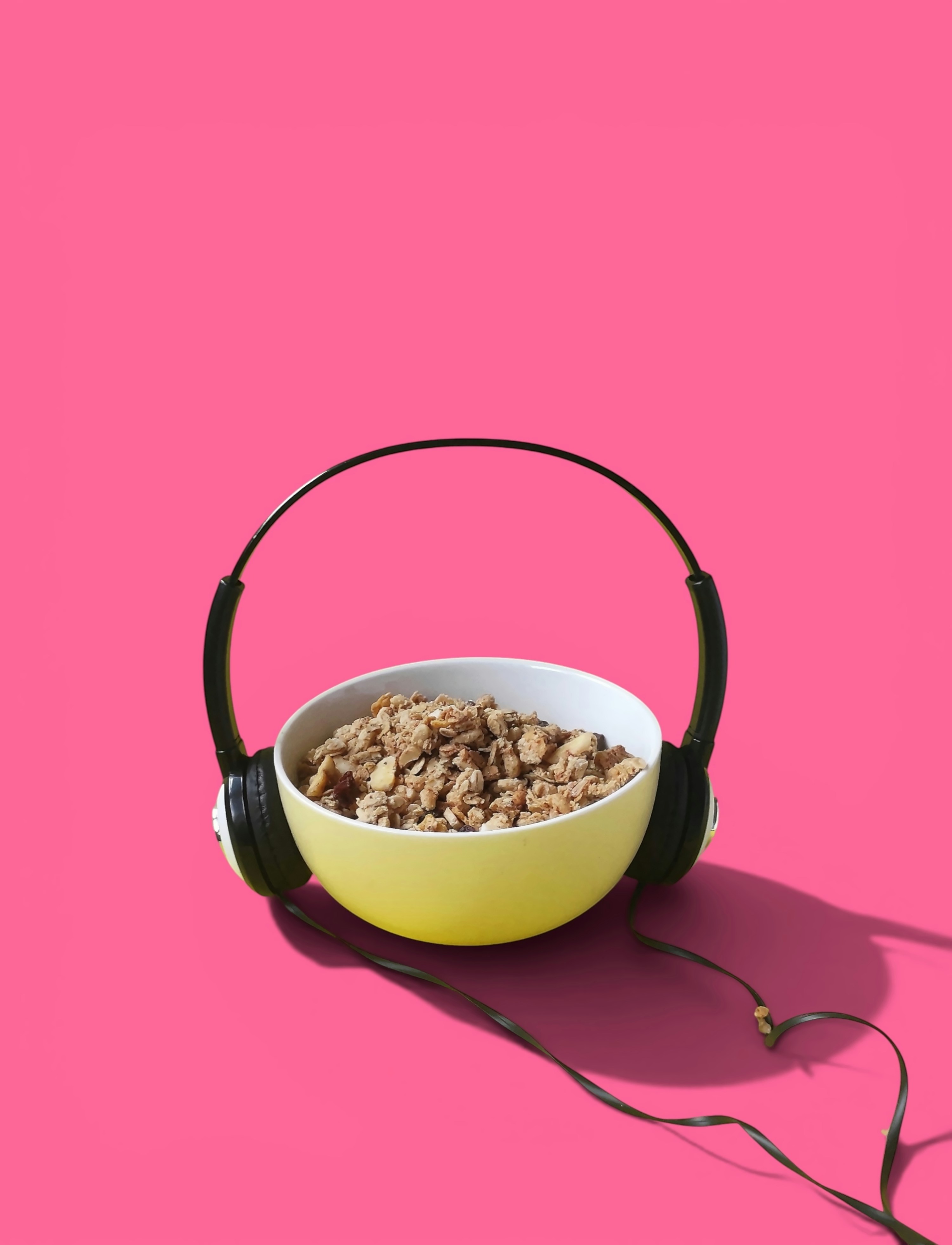 Yellow bowl of granola with headphones on a pink background