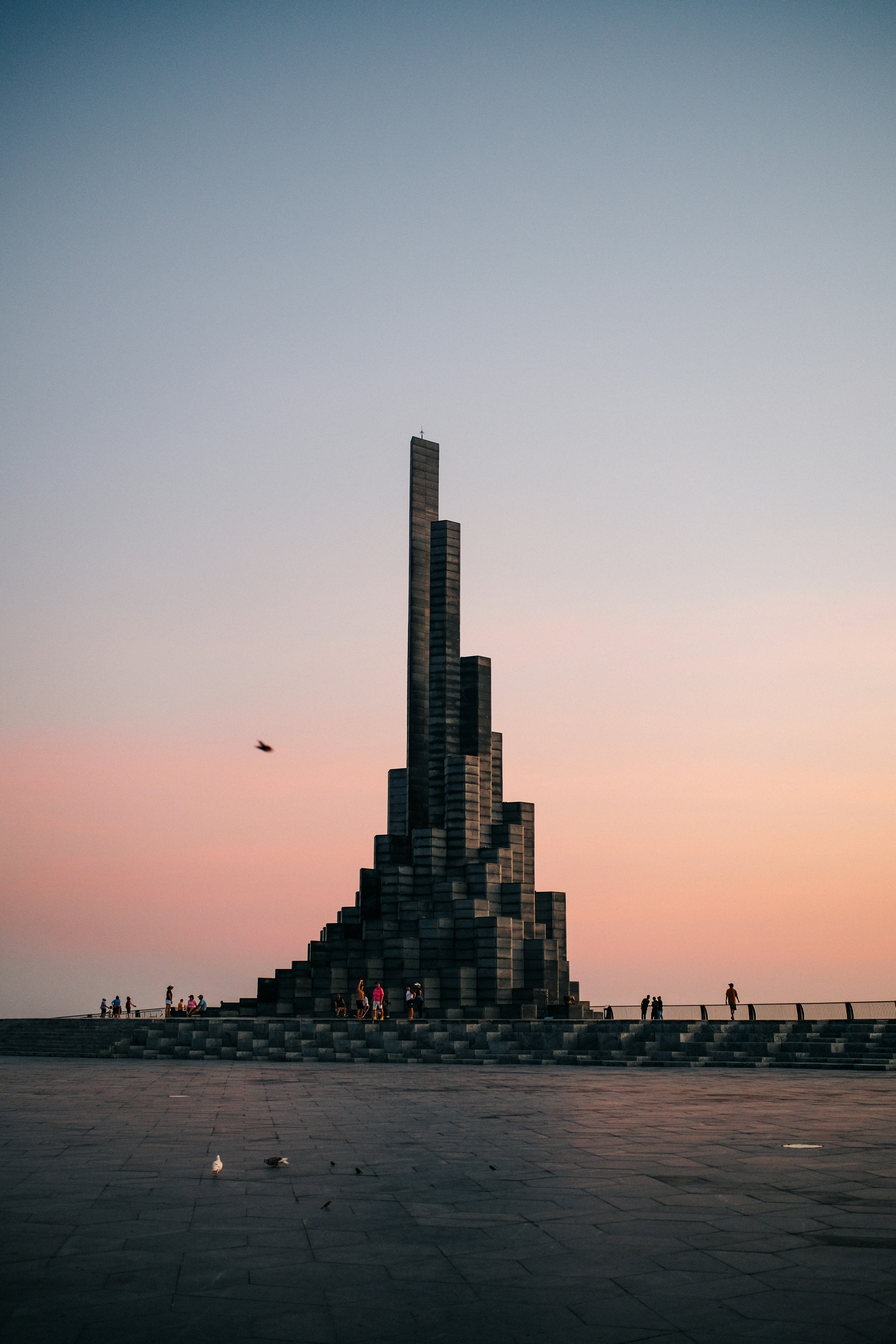 Uma escultura alta e moderna contra um céu pastel ao pôr do sol.