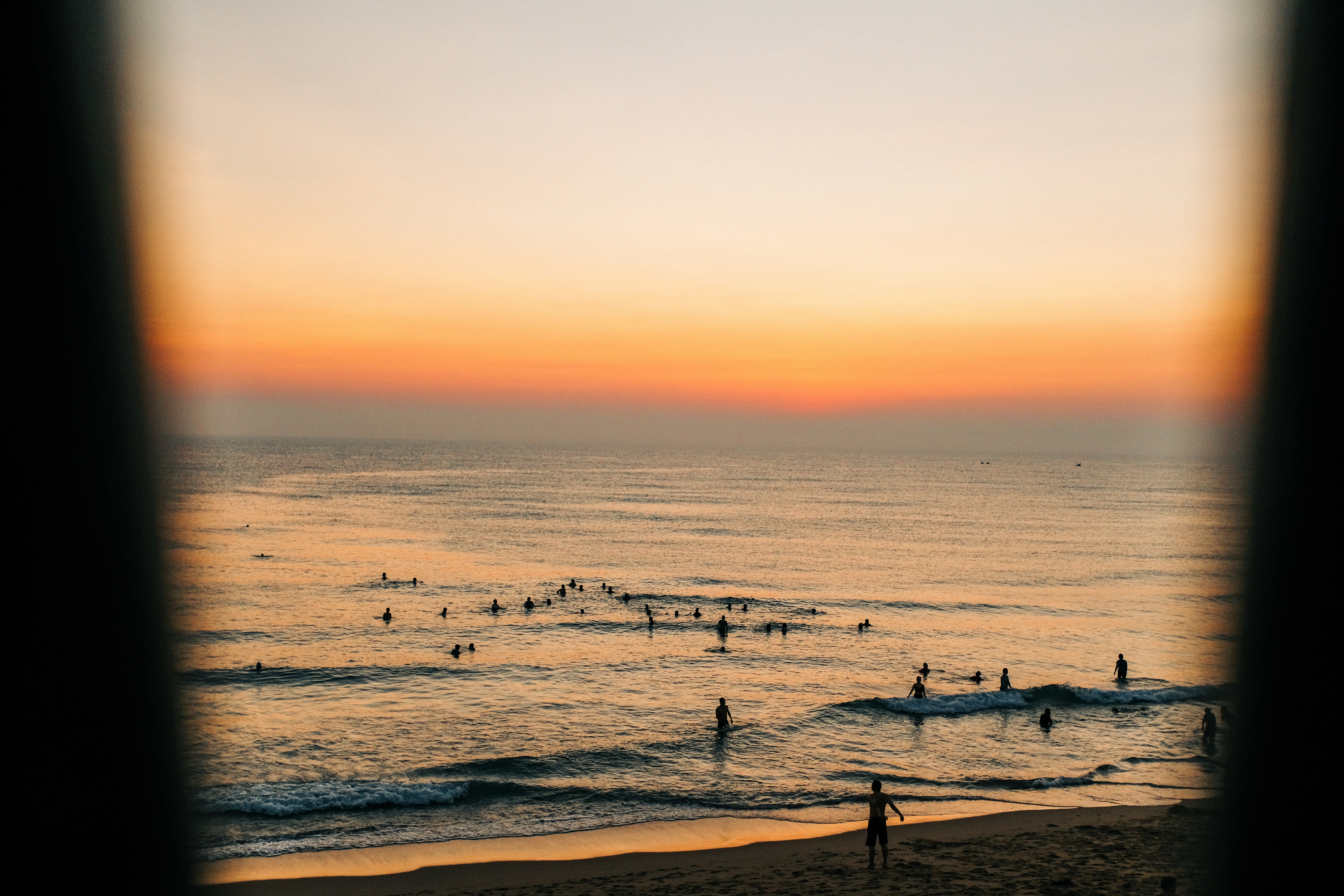 Surfistas surfando ondas ao pôr do sol em uma praia.