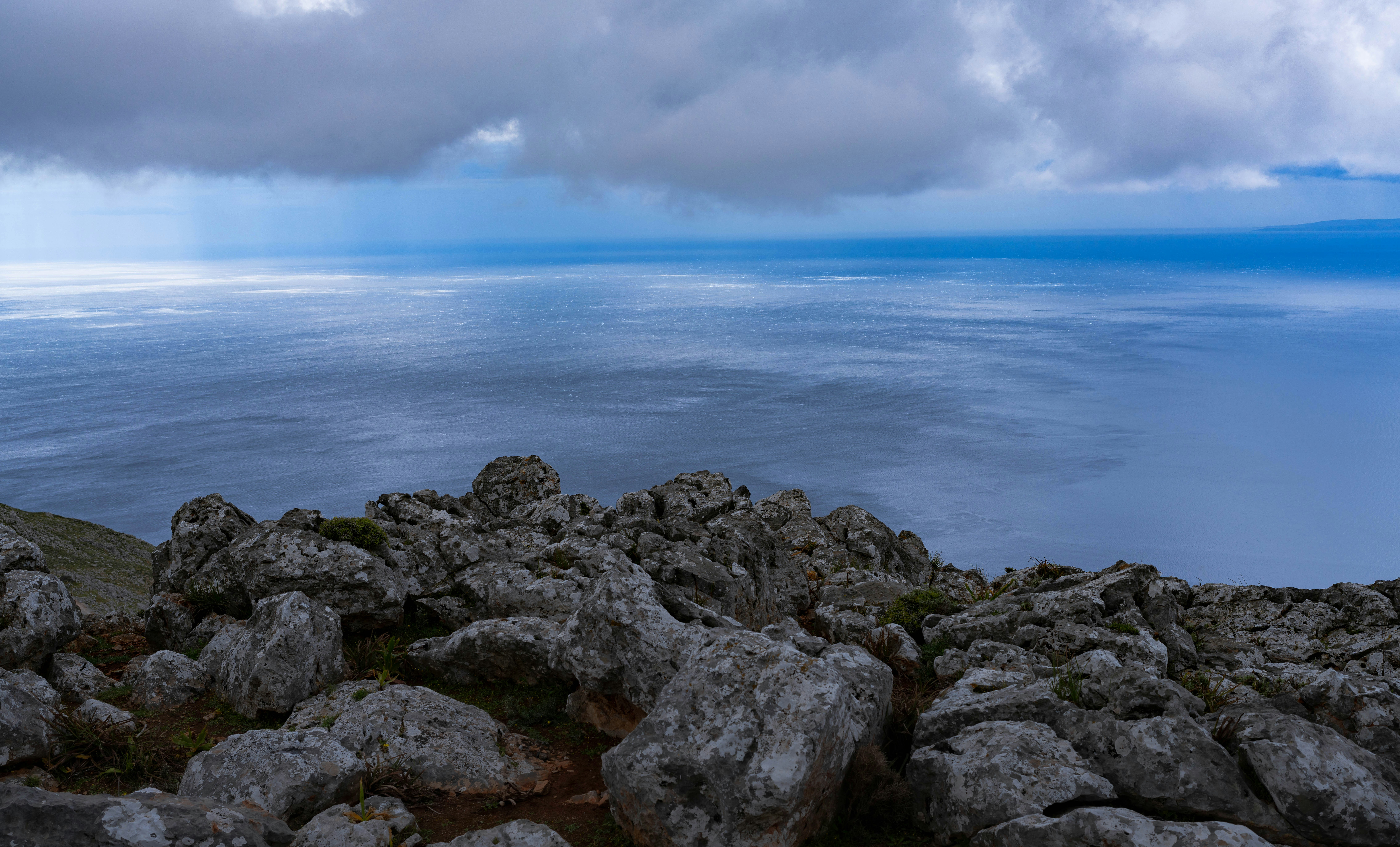Felsiger Vordergrund mit Blick auf einen weiten, ruhigen Ozean unter wolkigem Himmel