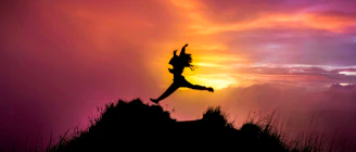 Silhouette of person jumping on a rocky cliff at sunset