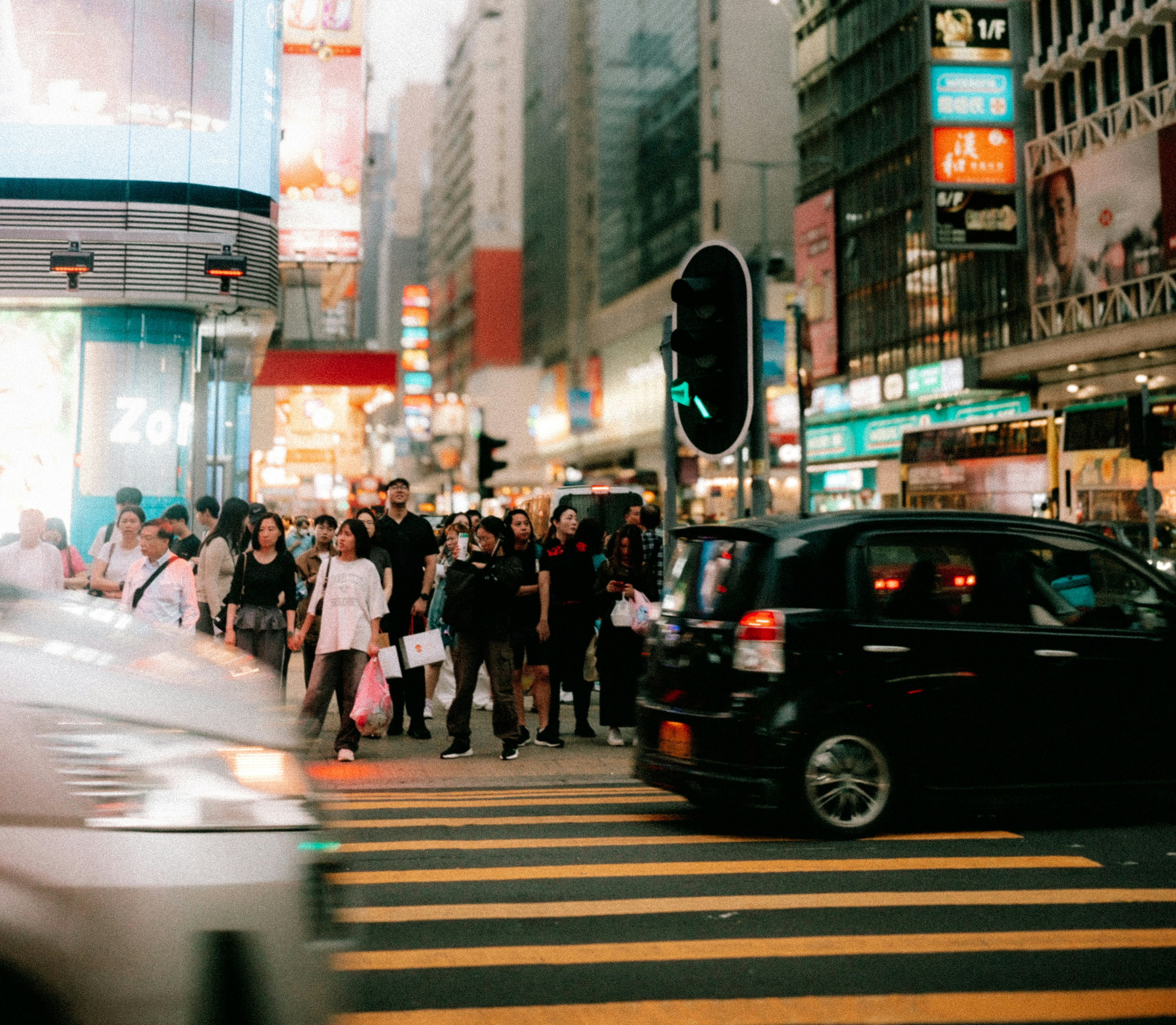 Pedestrians crossing a busy street at night with traffic lights.