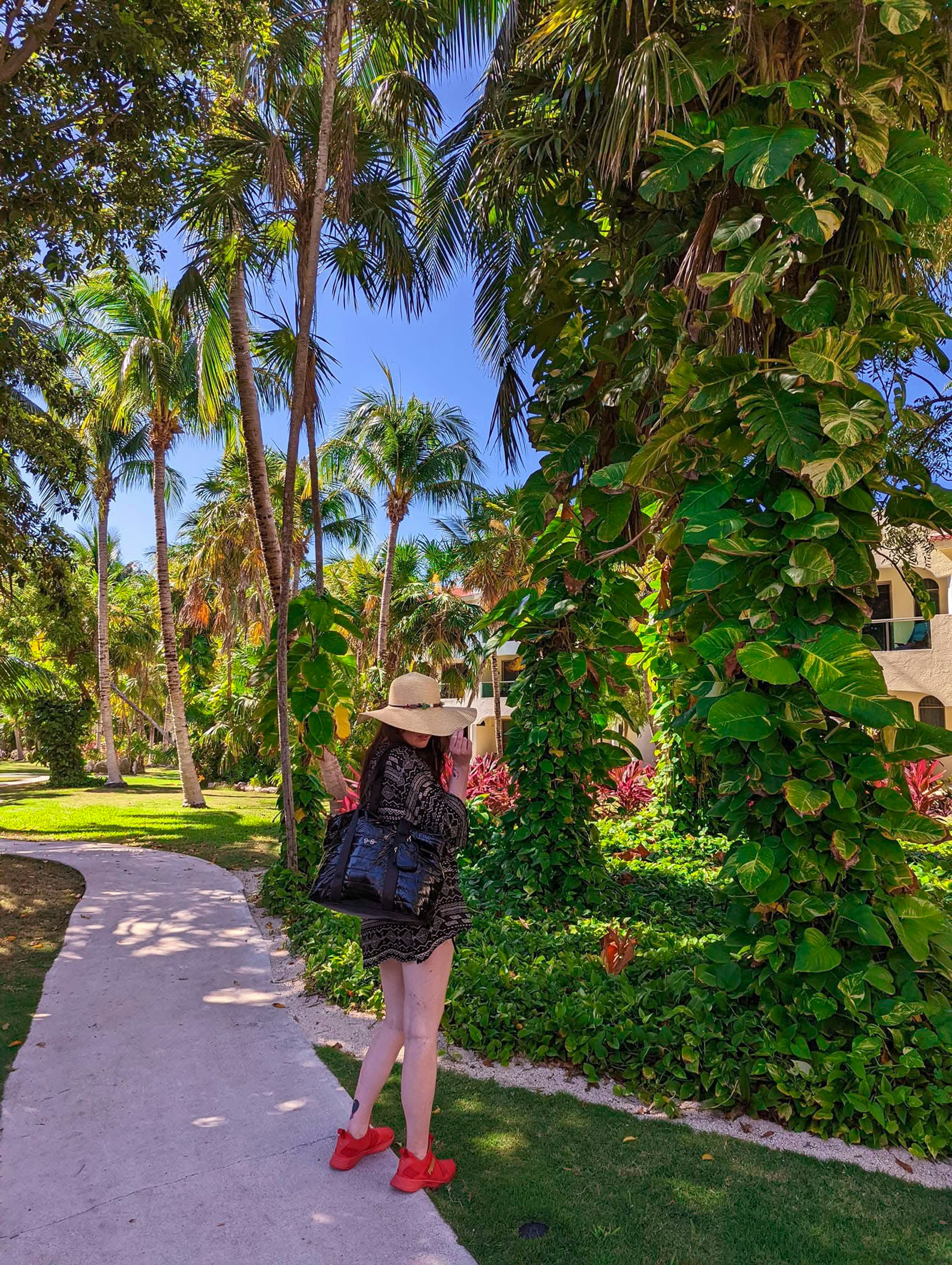 Woman in hat walks on path through lush tropical garden