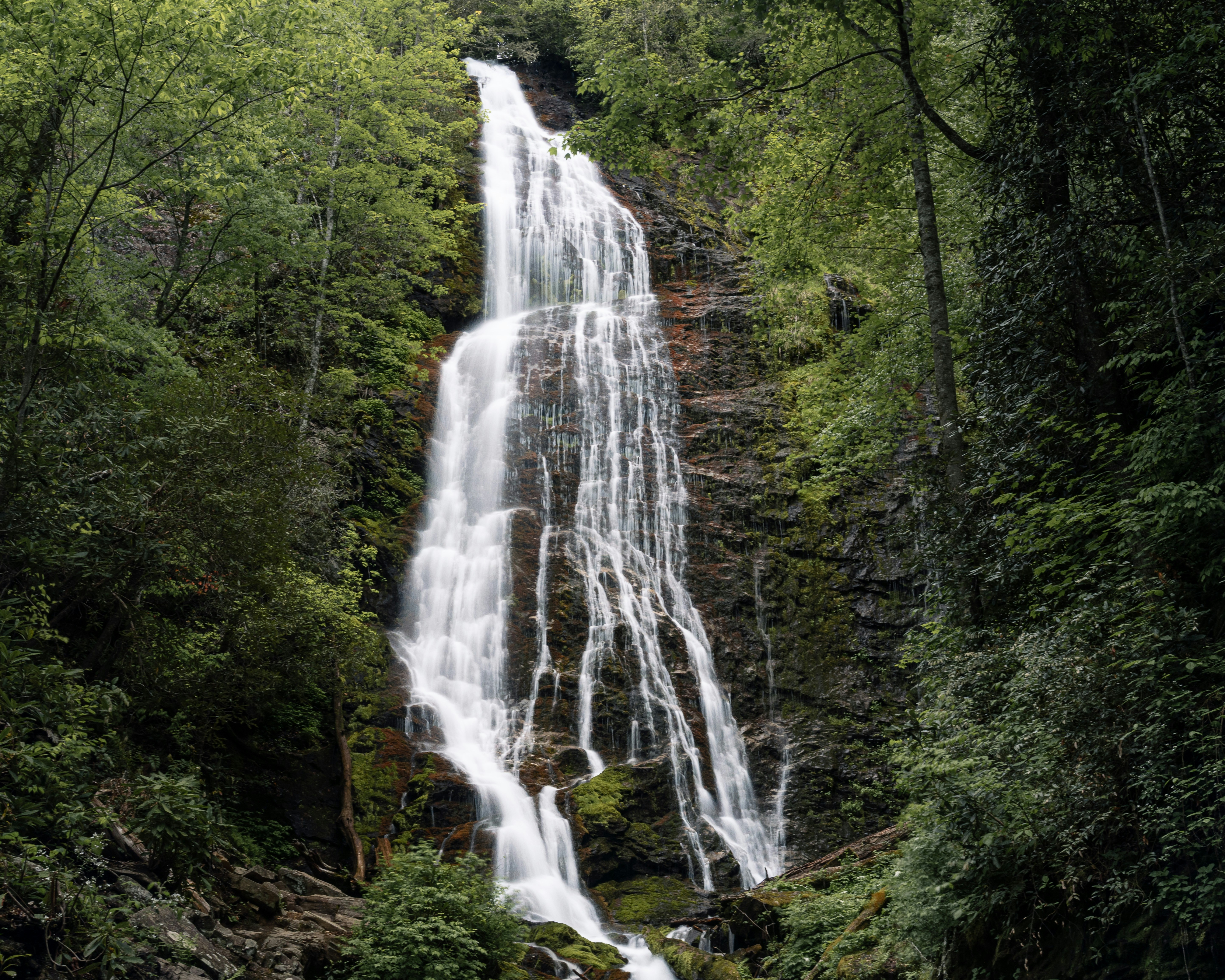 Uma alta cachoeira desce por uma face rochosa de um penhasco.