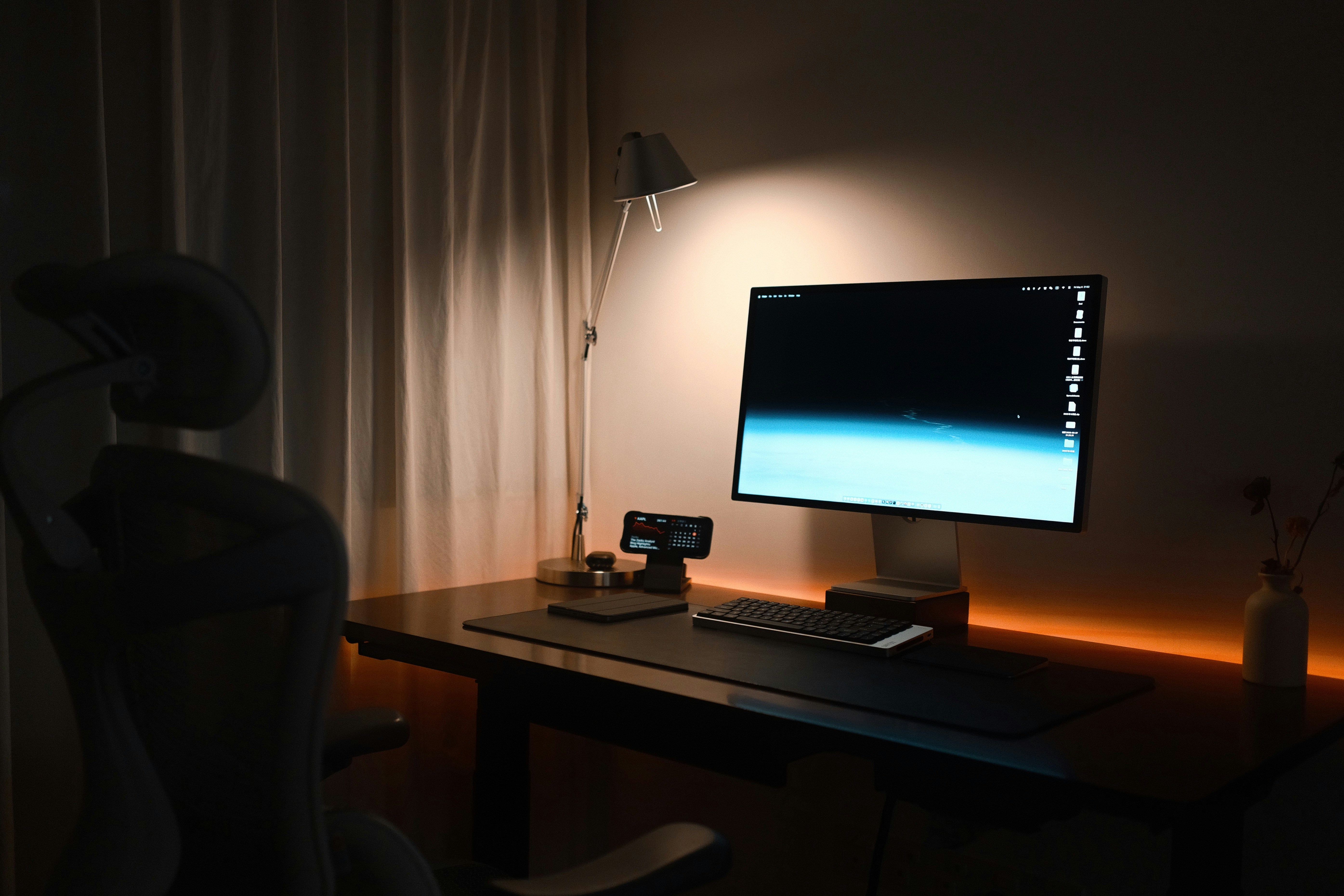 A dimly lit desk with a computer monitor and chair.