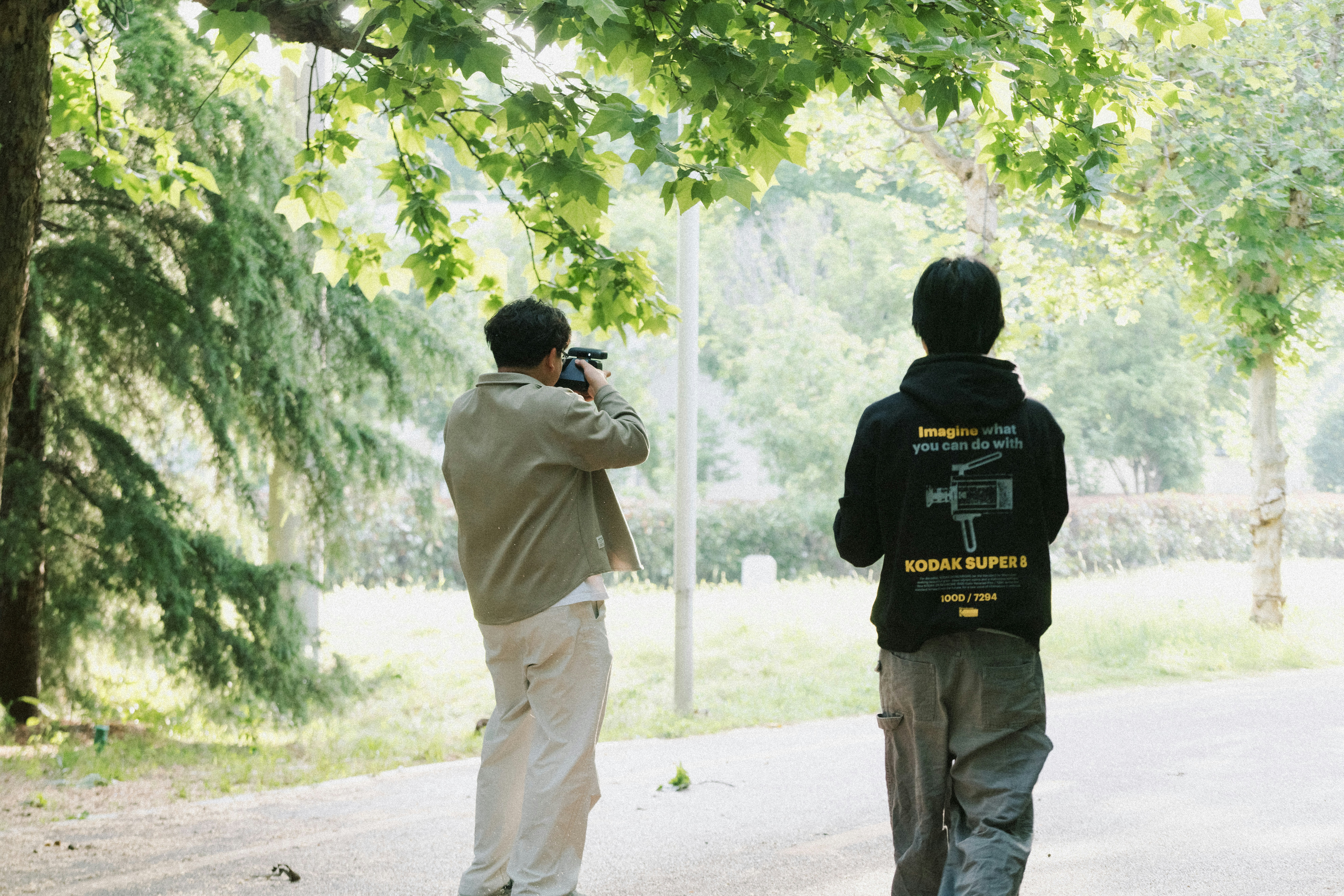 Two people filming in a park with trees