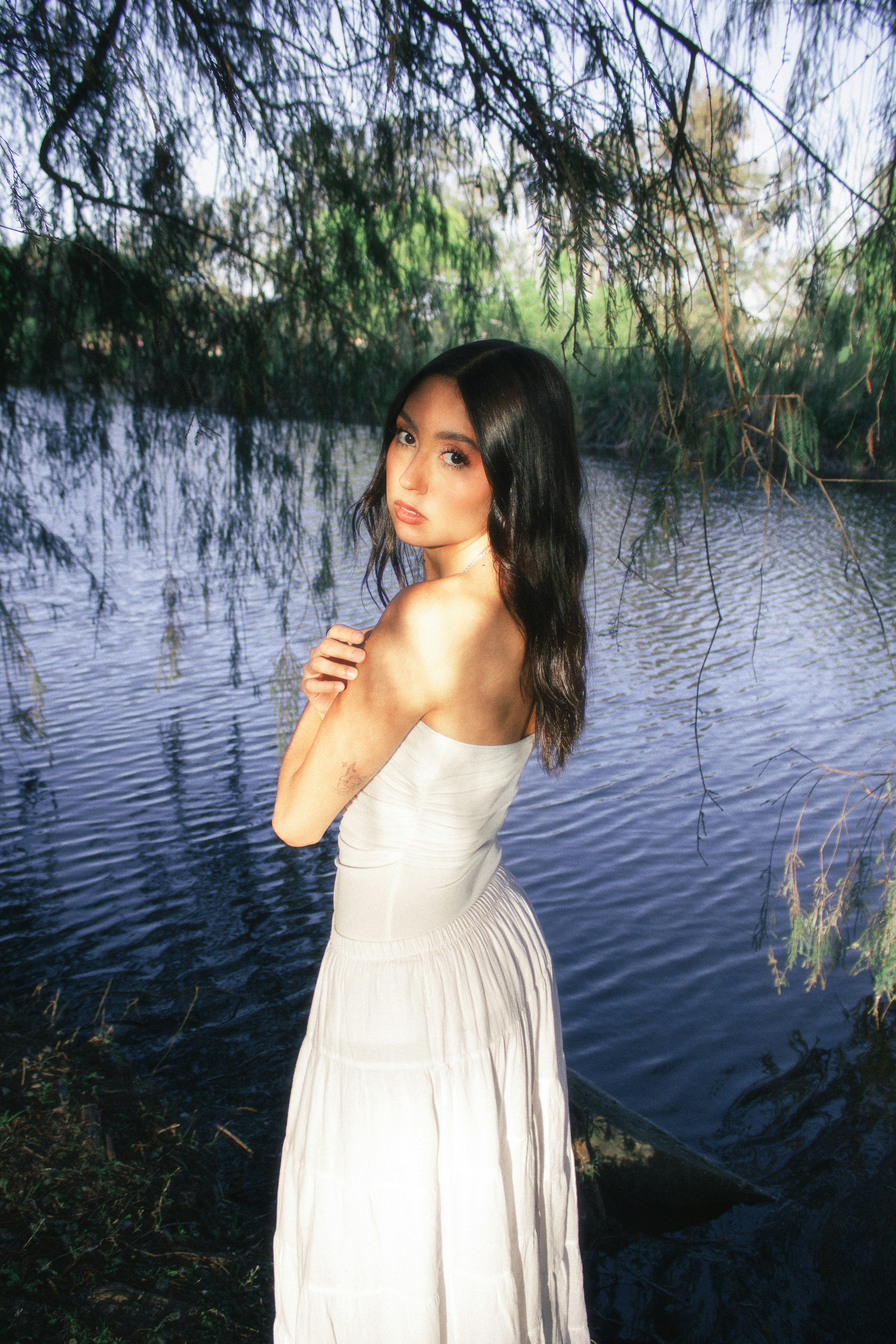 Young woman in white dress beside a tranquil lake.