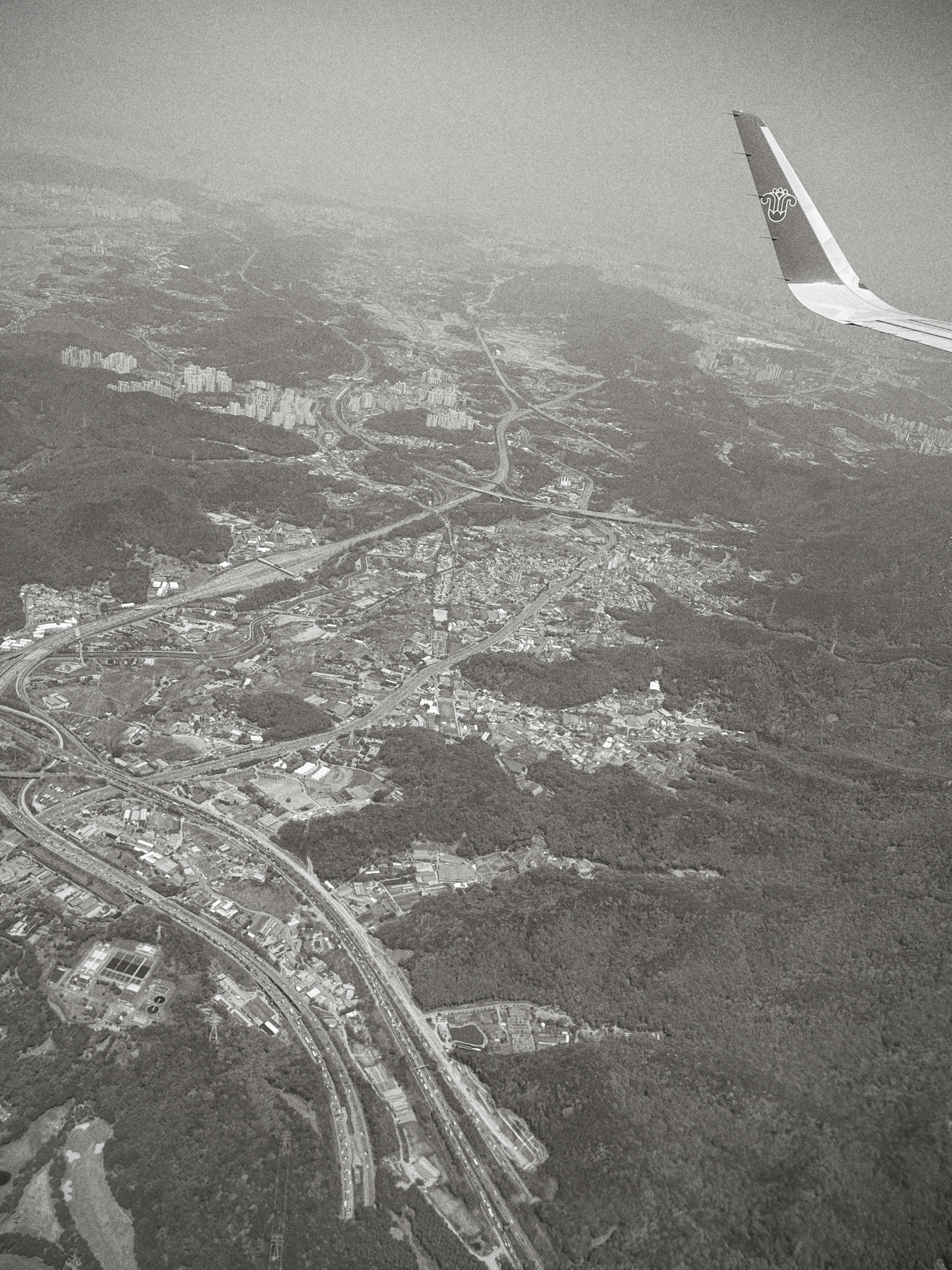 Monochrome aerial view of city, highways, and airplane wing.