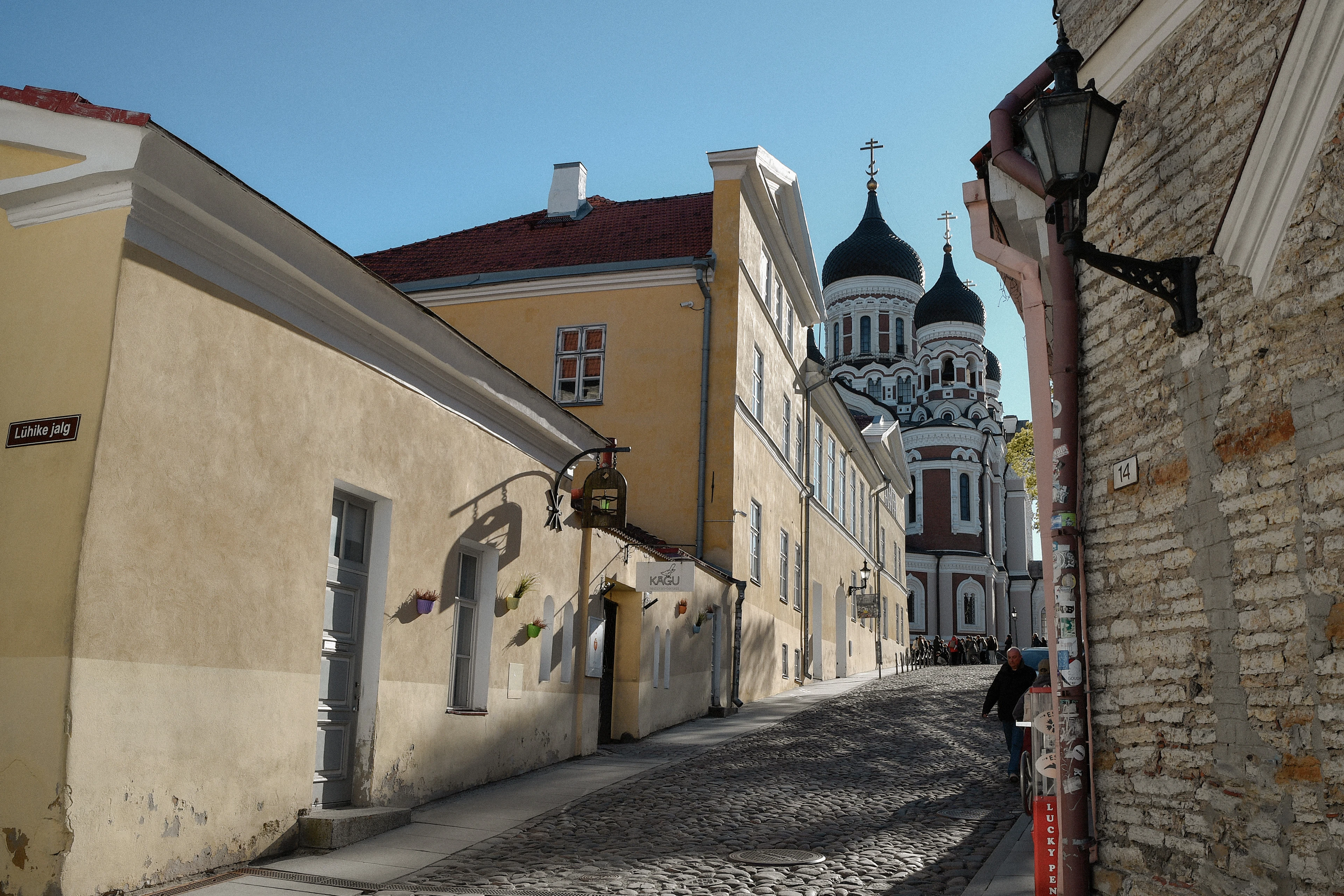 A cobbled lane on Tallinn's Toompea hill running between whitewashed old walls toward the black onion domes of Alexander Nevsky Cathedral.