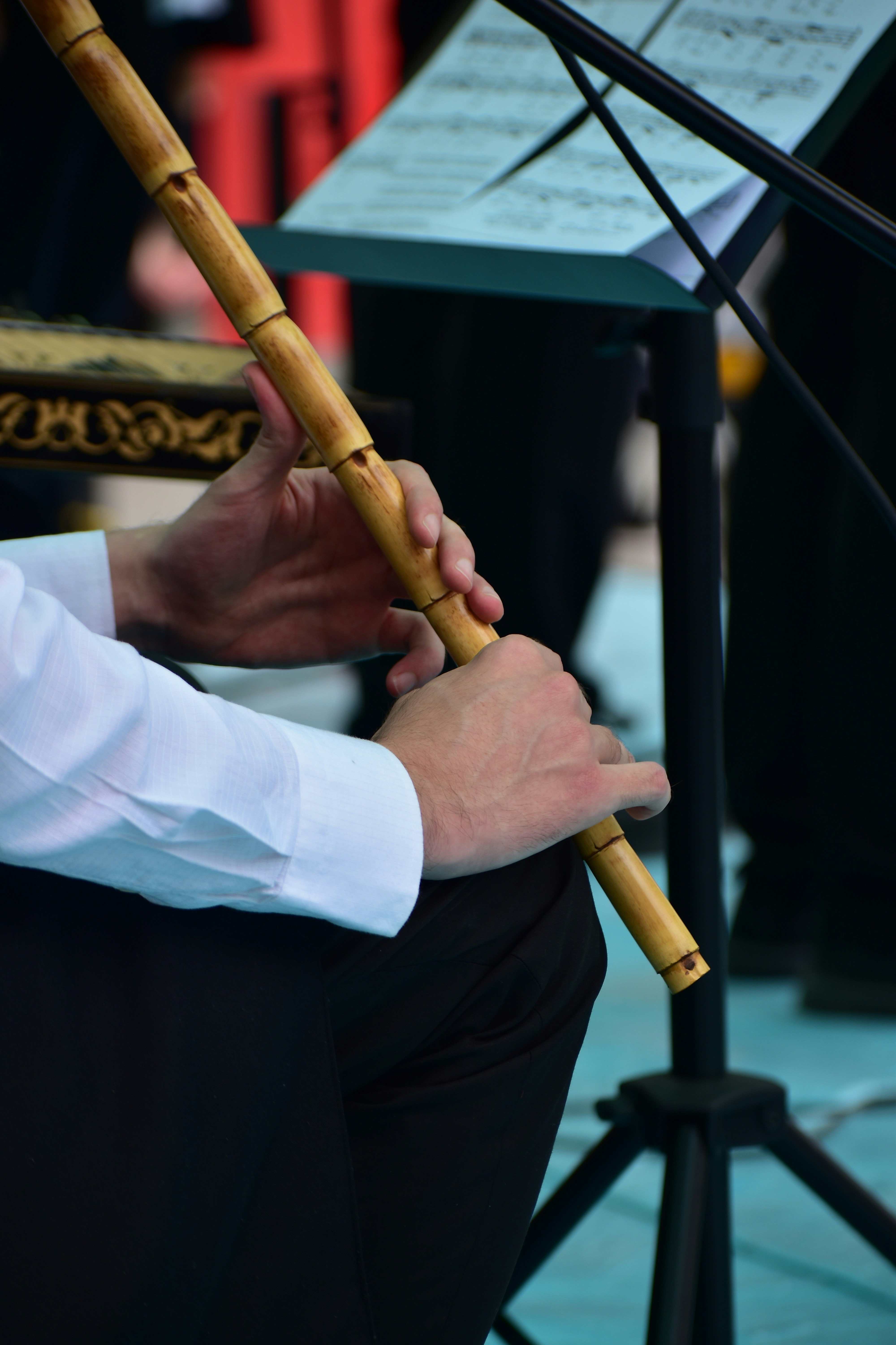 Mãos de músico tocando um instrumento de sopro de madeira com partituras.