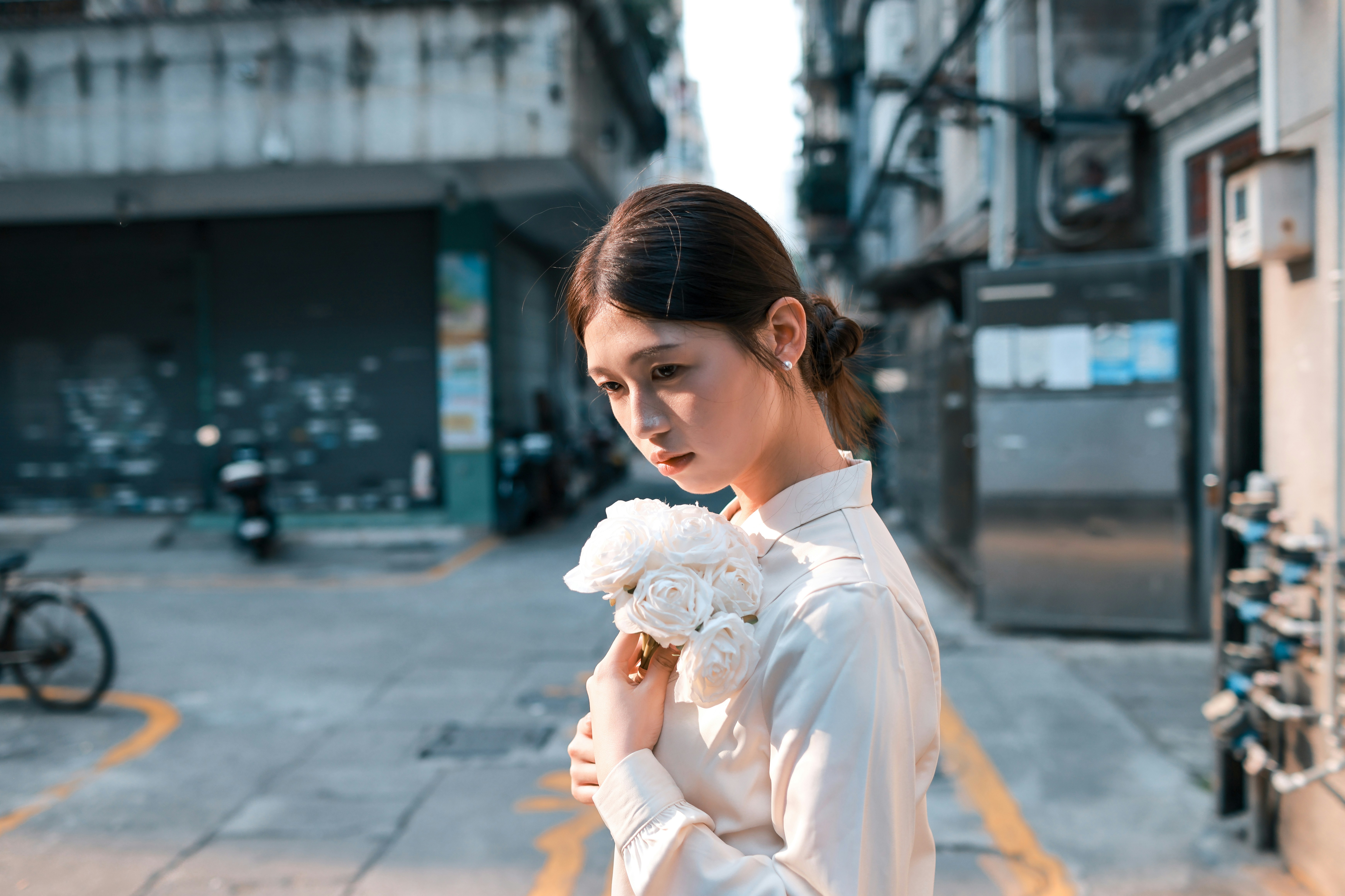 Young woman holding white flowers in an urban alley.