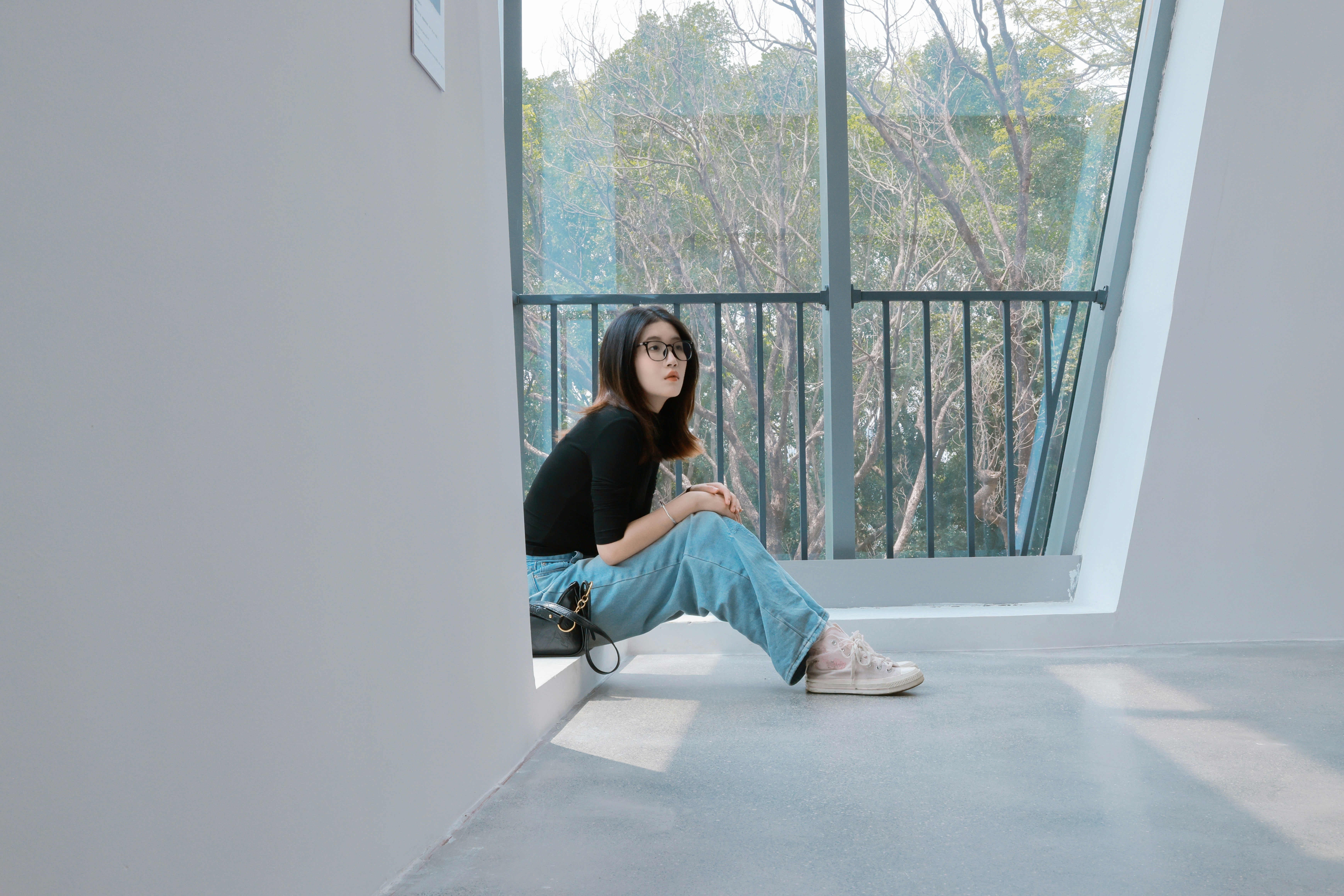 A woman sitting by a large window with trees outside