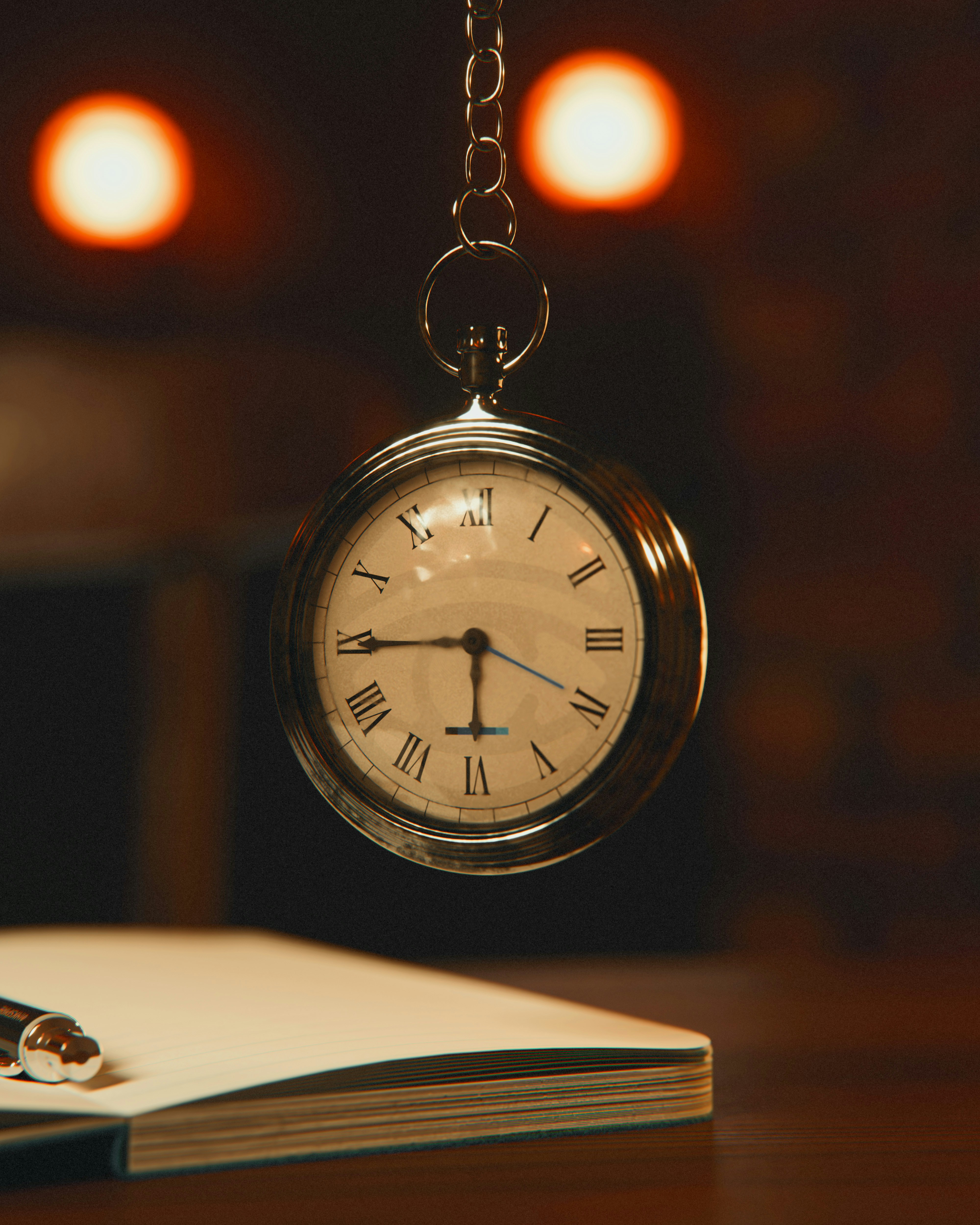 A silver pocket watch hangs above a notebook and pen