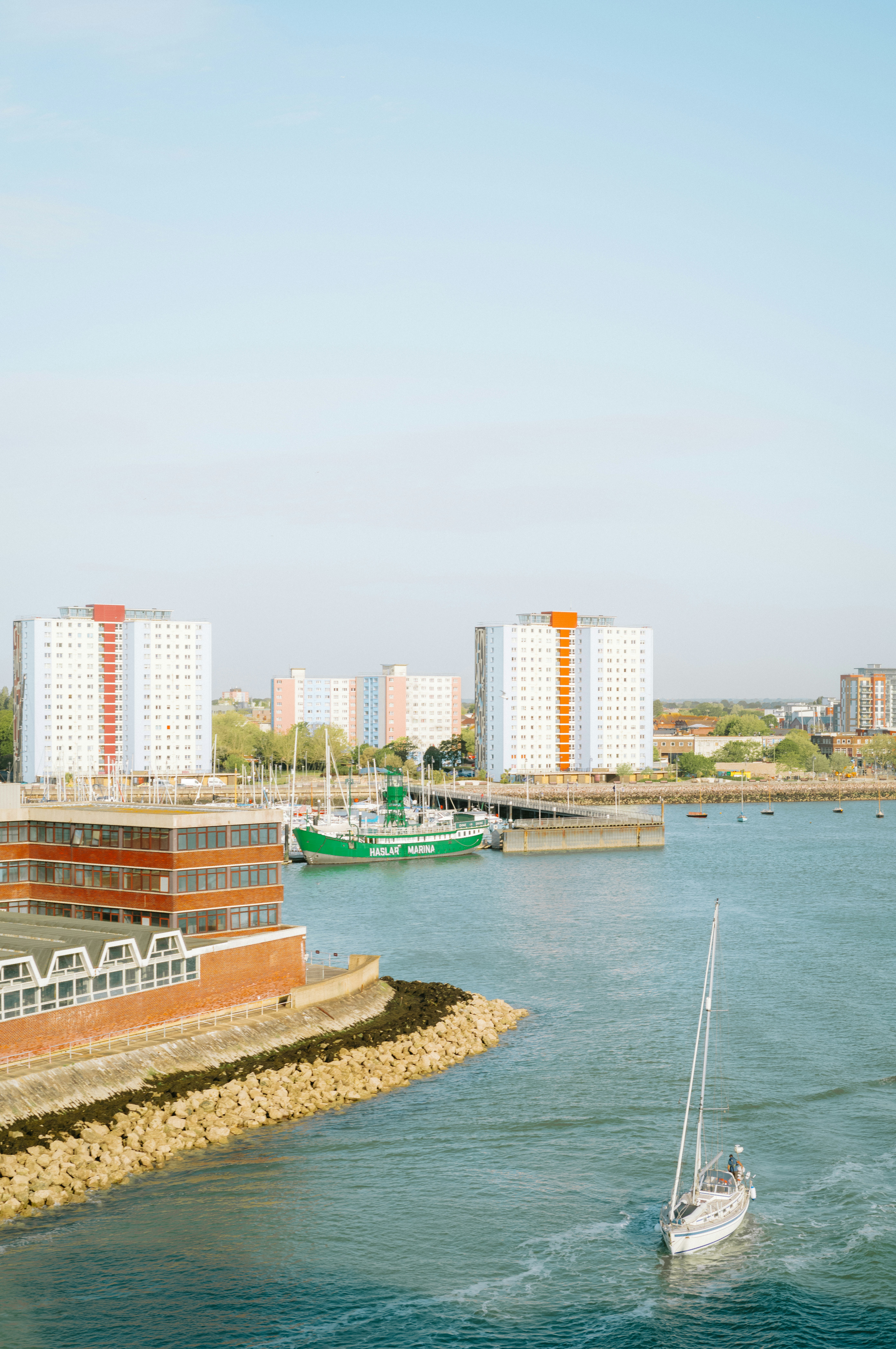 Sailboat on the water near buildings and a green boat. - 相关推荐
