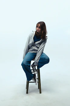 Young woman in jeans and hoodie sits on stool