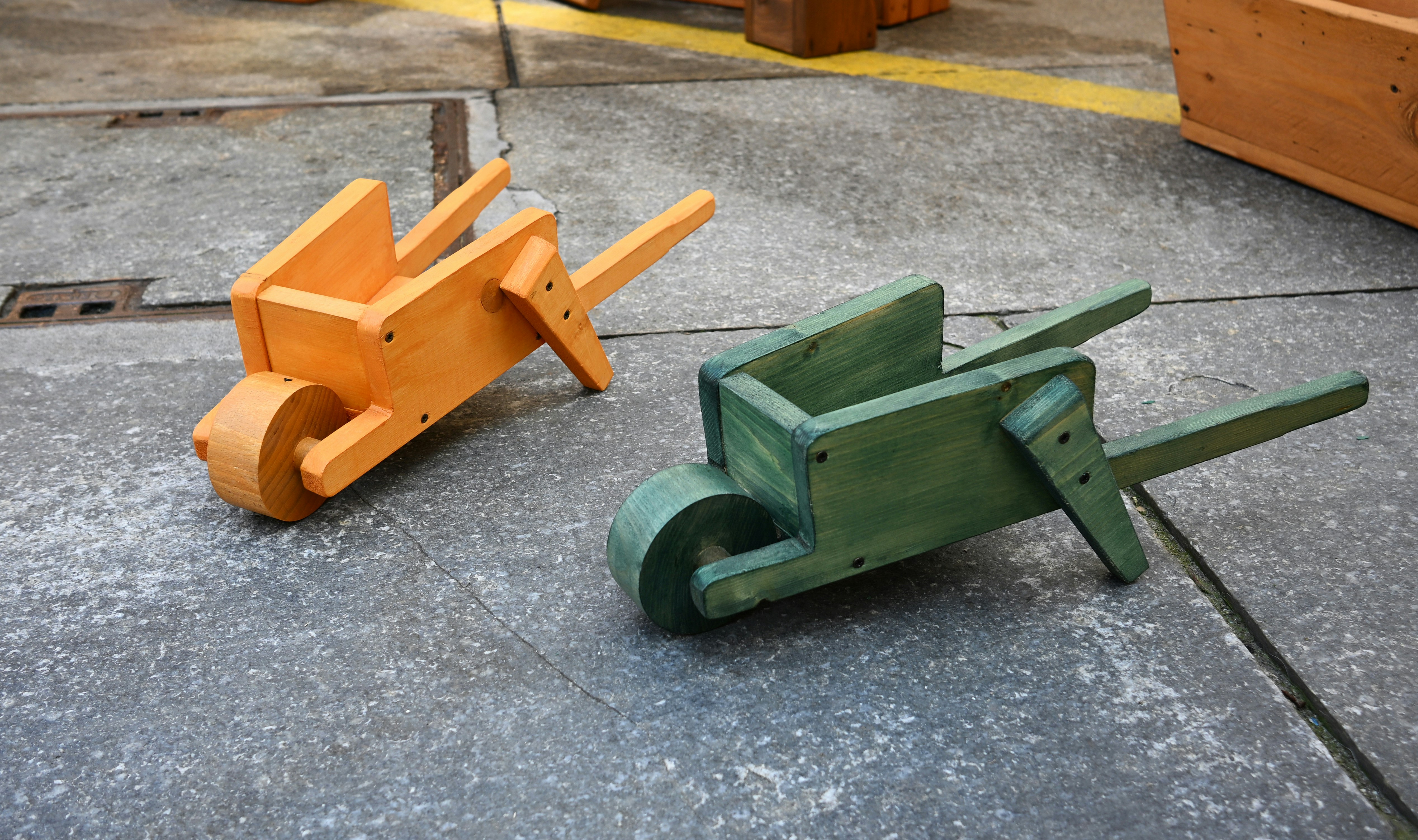 Deux brouettes jouets en bois colorées posées sur une surface en béton.