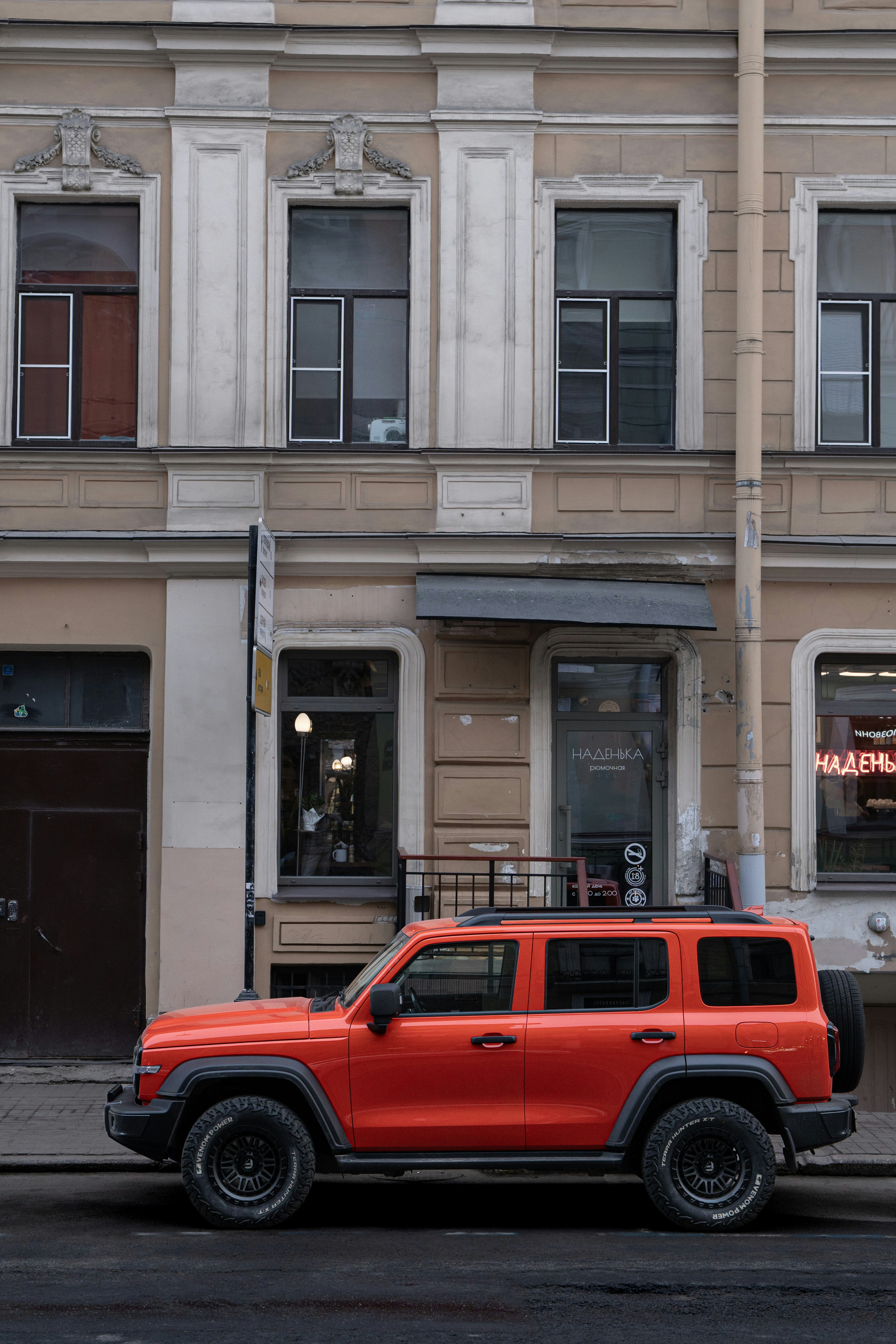 Un SUV arancione vivace parcheggiato accanto a un vecchio edificio.