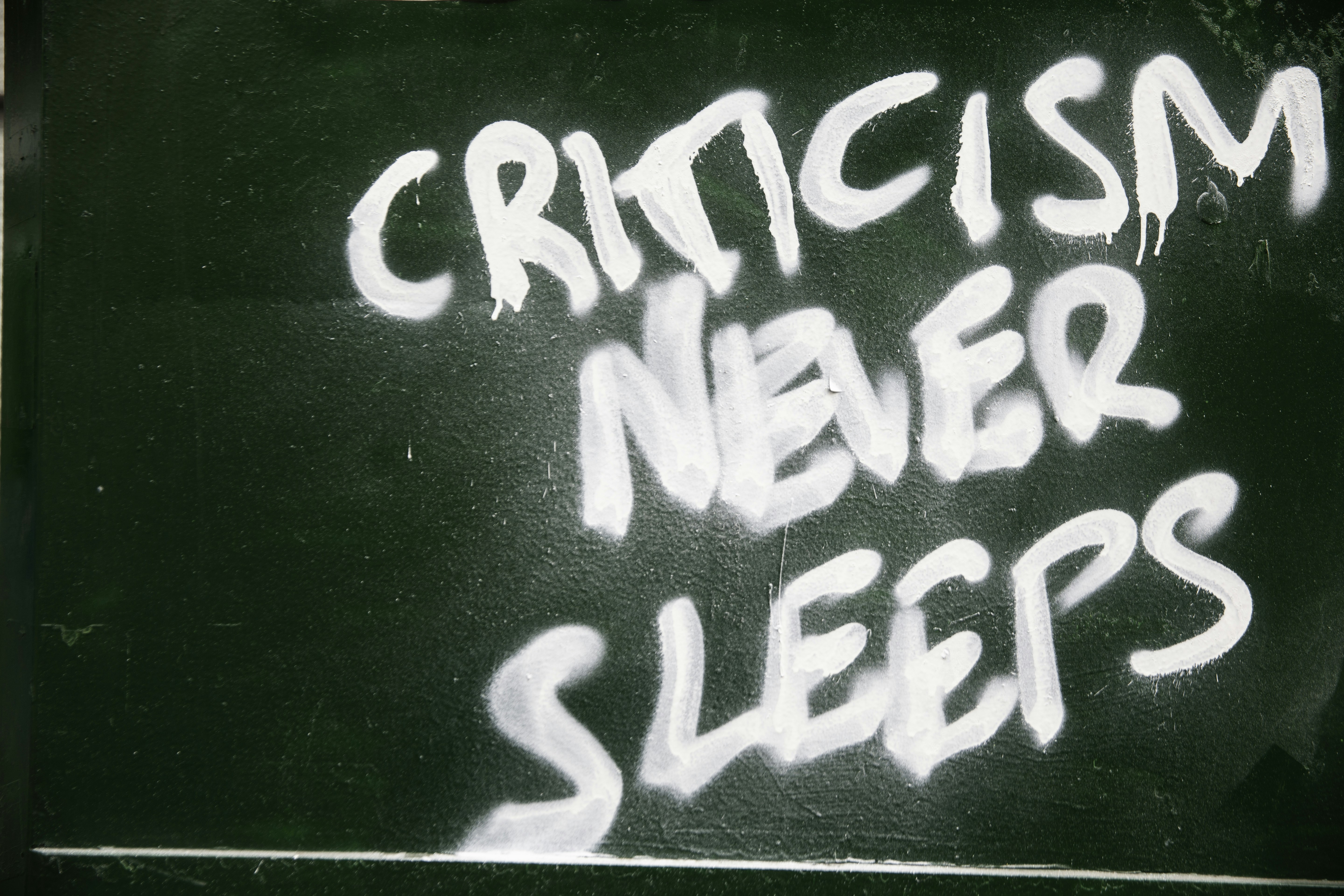 Grafiti di dinding hijau bertuliskan "kritik tidak pernah tidur"