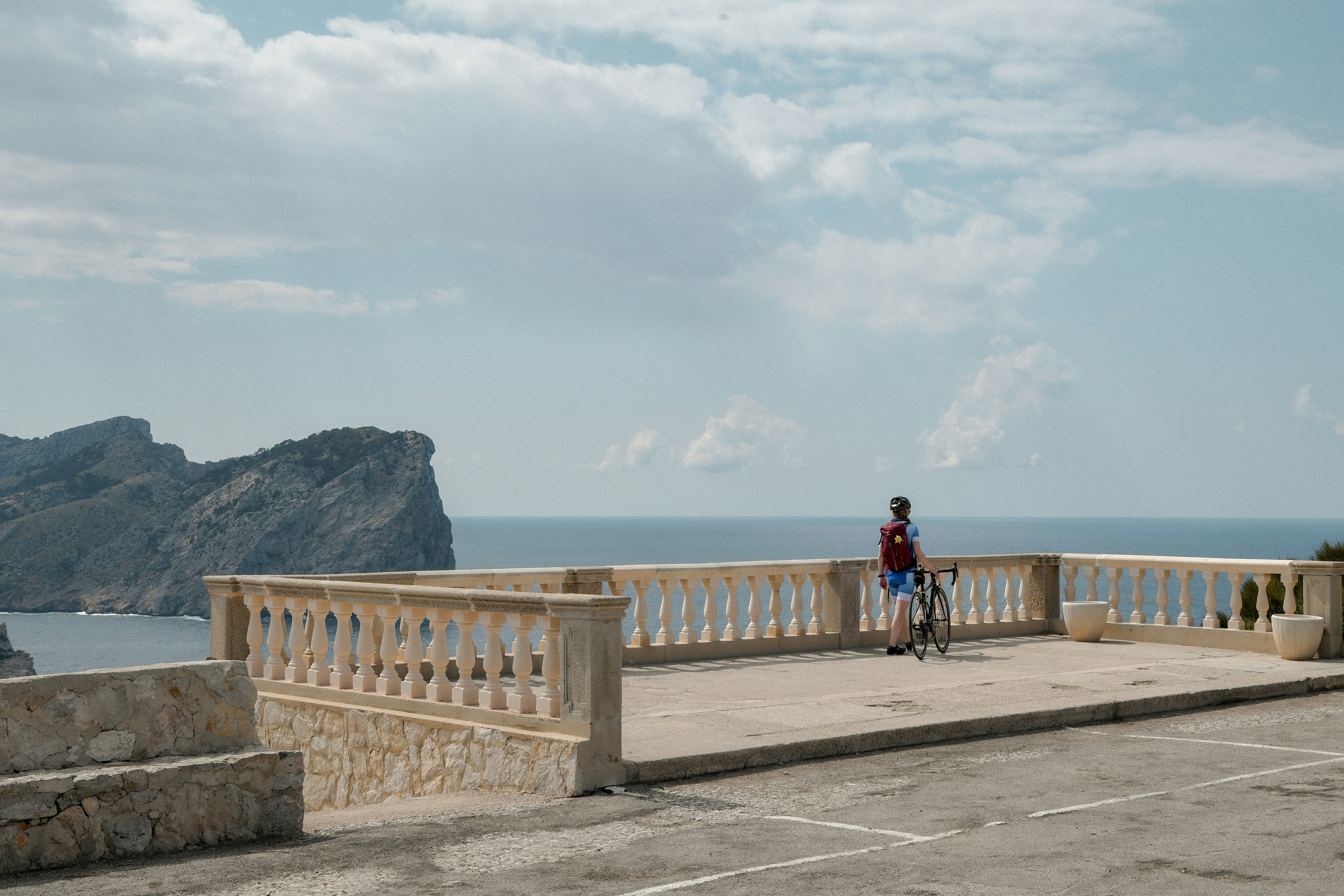Person with bicycle on a balcony overlooking ocean and cliffs.