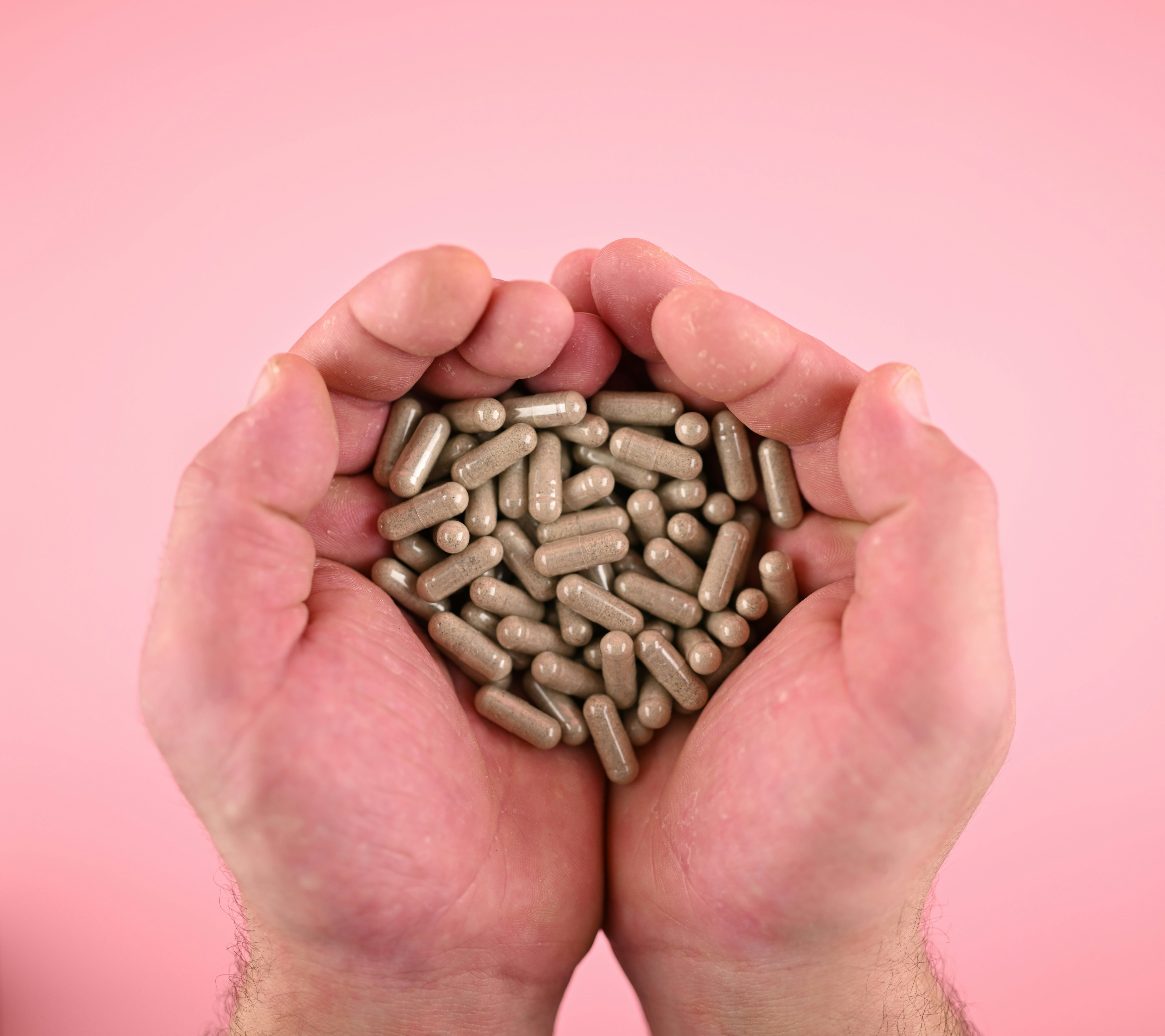 Mani che tengono numerose capsule grigie su uno sfondo rosa.