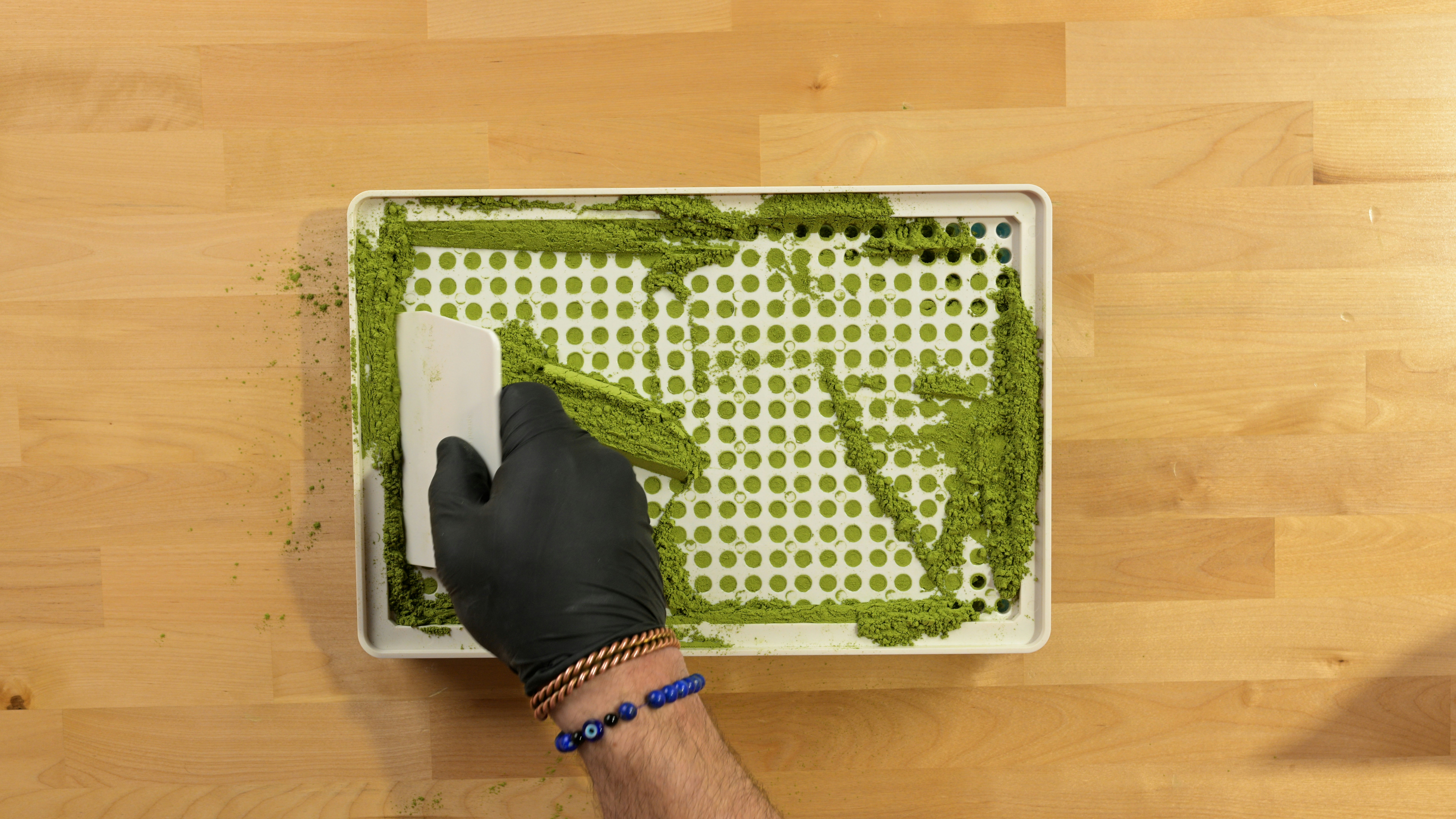 Hand spreading green paste on a white tray