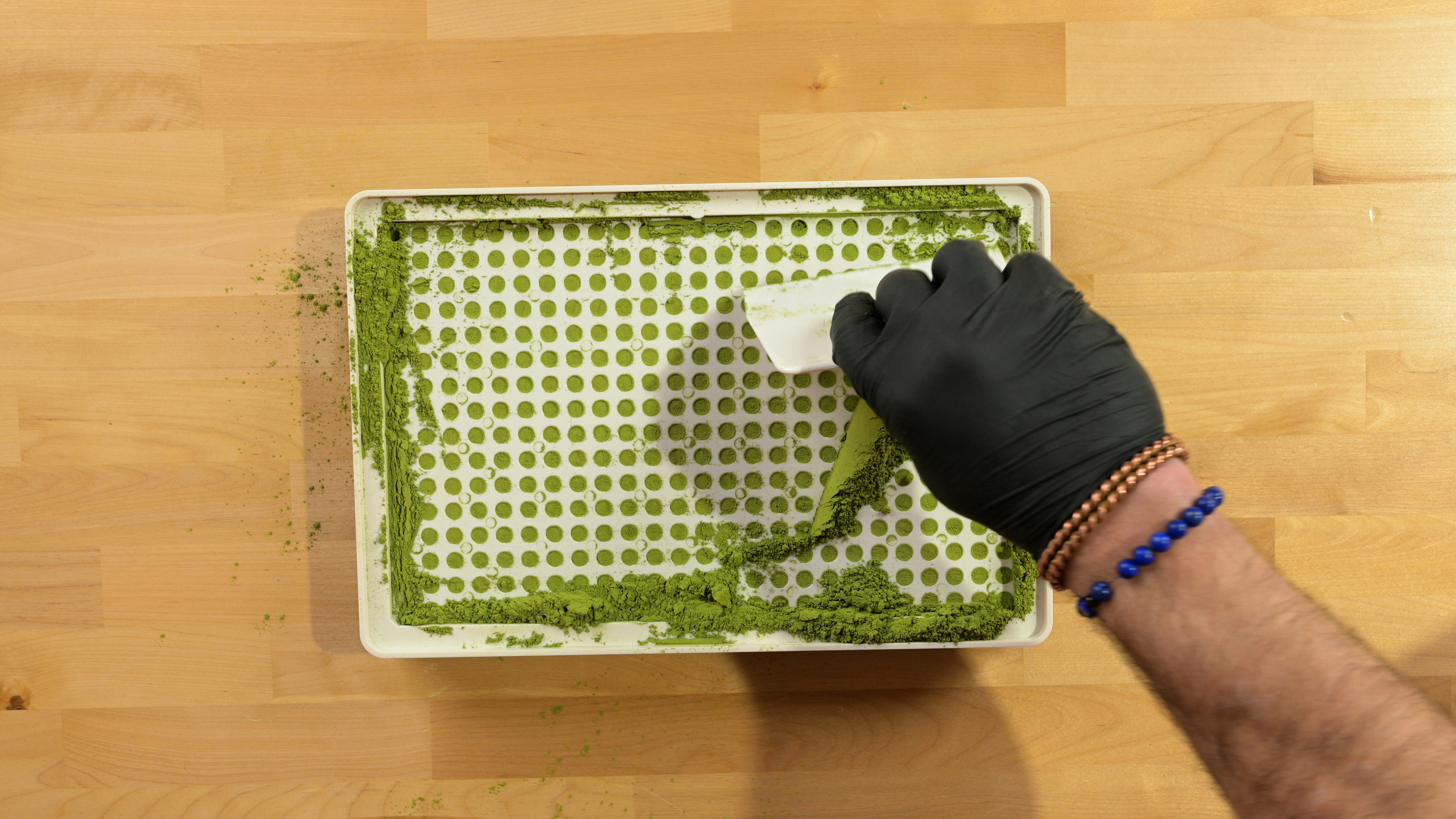 Spreading herbal green powder into empty capsules using a Cap & Press™ Core Series 400 Hole capsule filling machine from a top overhead view - Photo courtesy of https://blated.com - credit appreciated