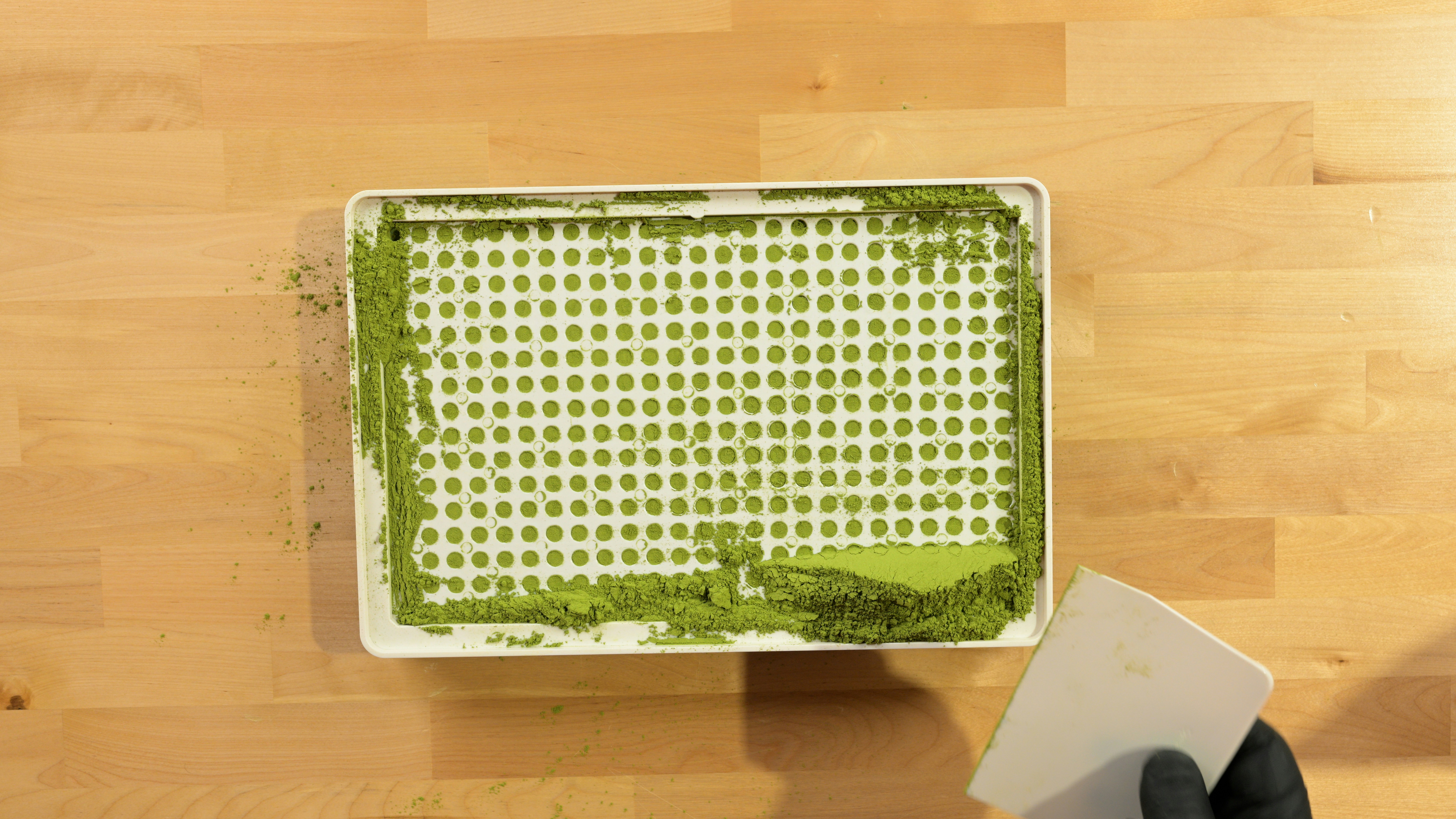 Green powder being spread on a tray