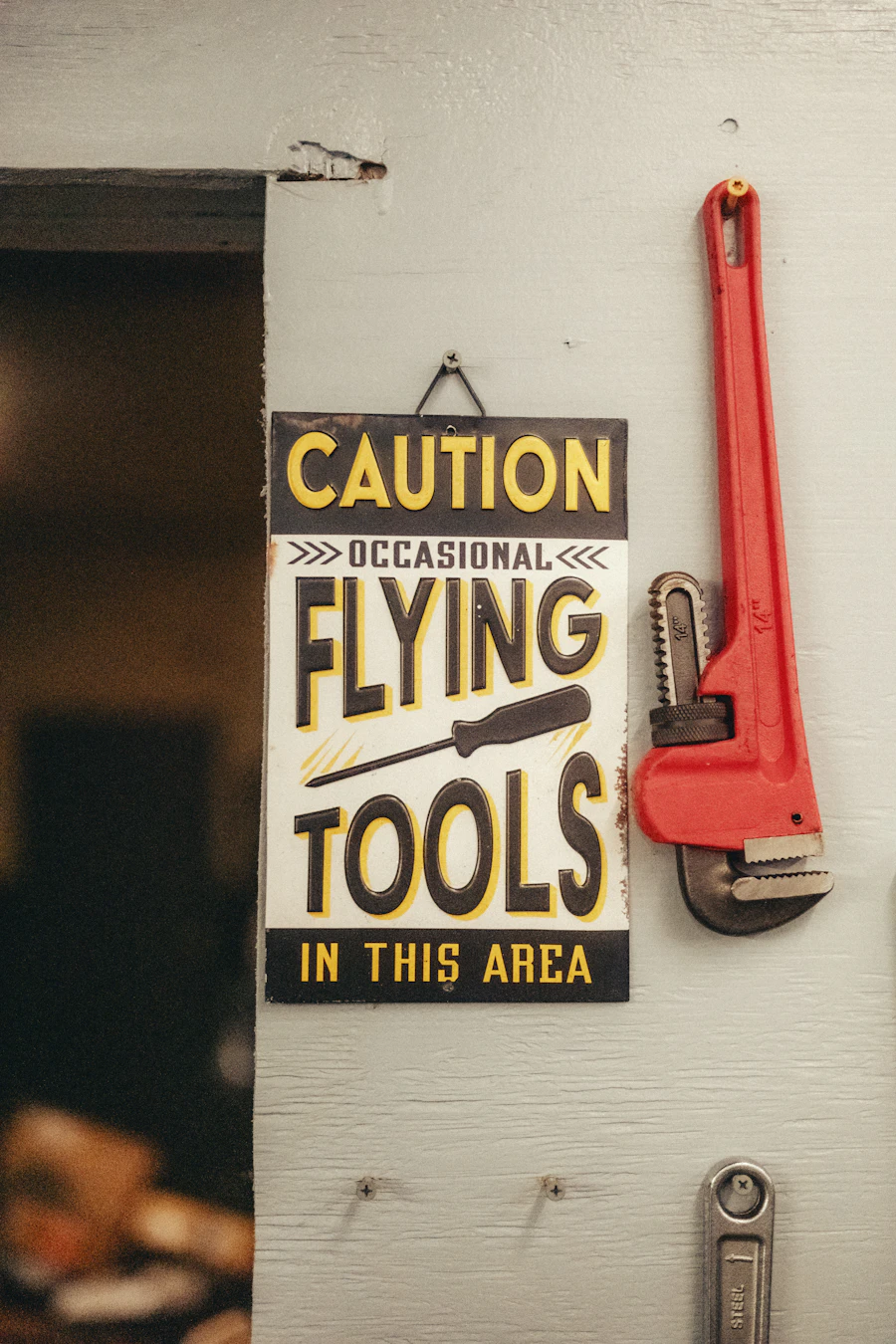 A red pipe wrench hanging beside a sign reading Caution: Occasional Flying Tools