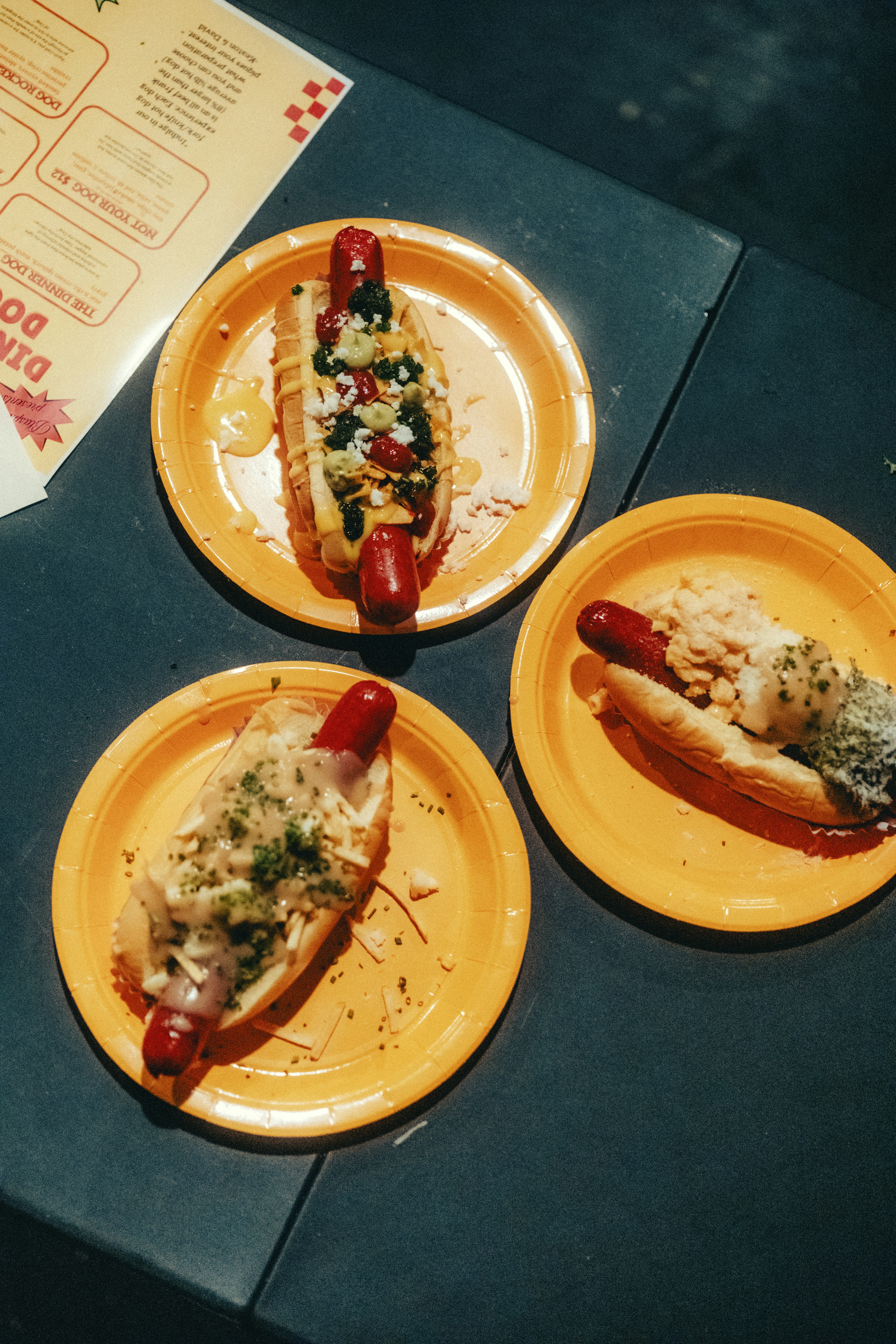 Three loaded hot dogs on yellow plates