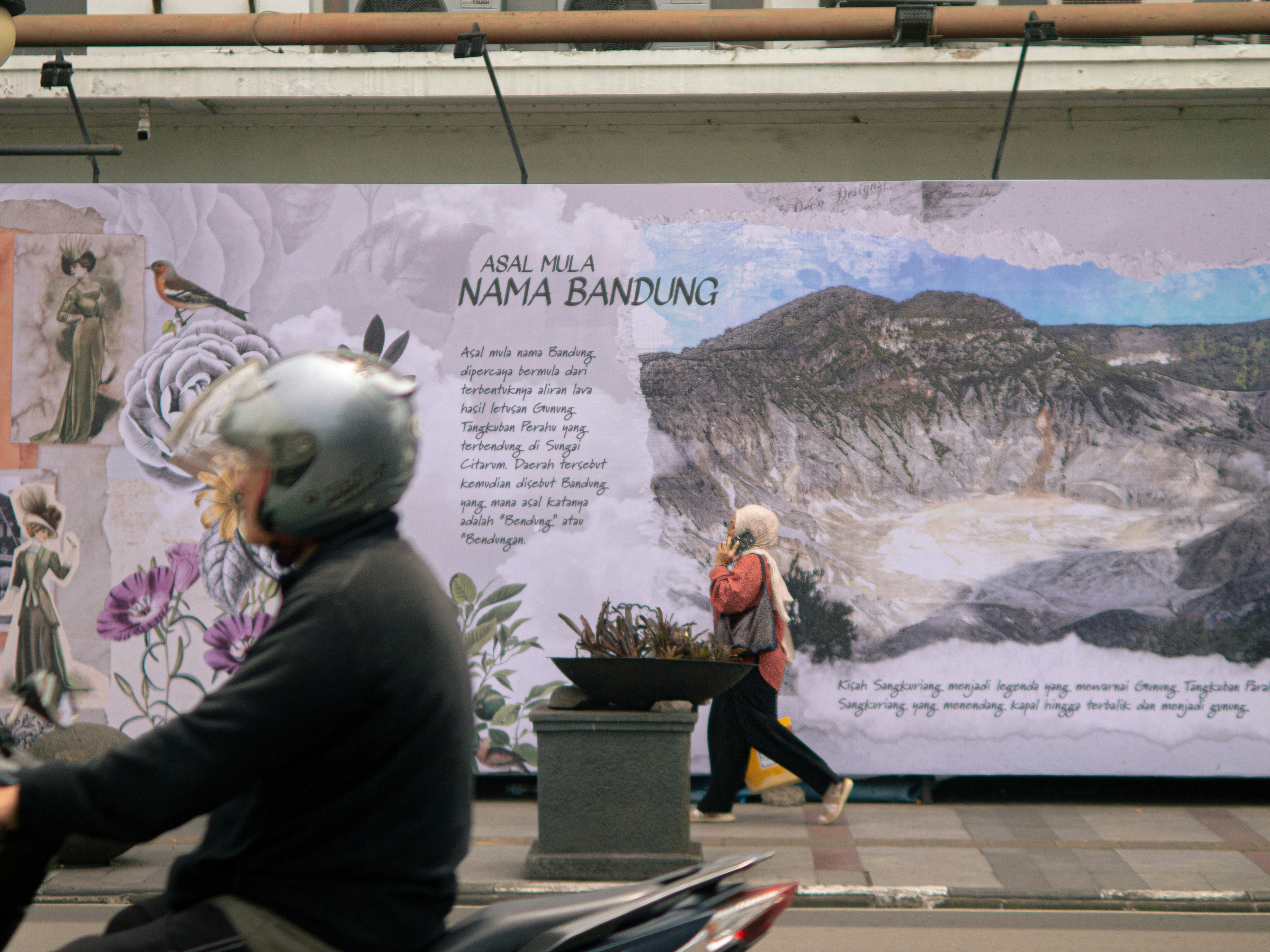 Orang-orang berjalan melewati mural yang menggambarkan lanskap pegunungan.