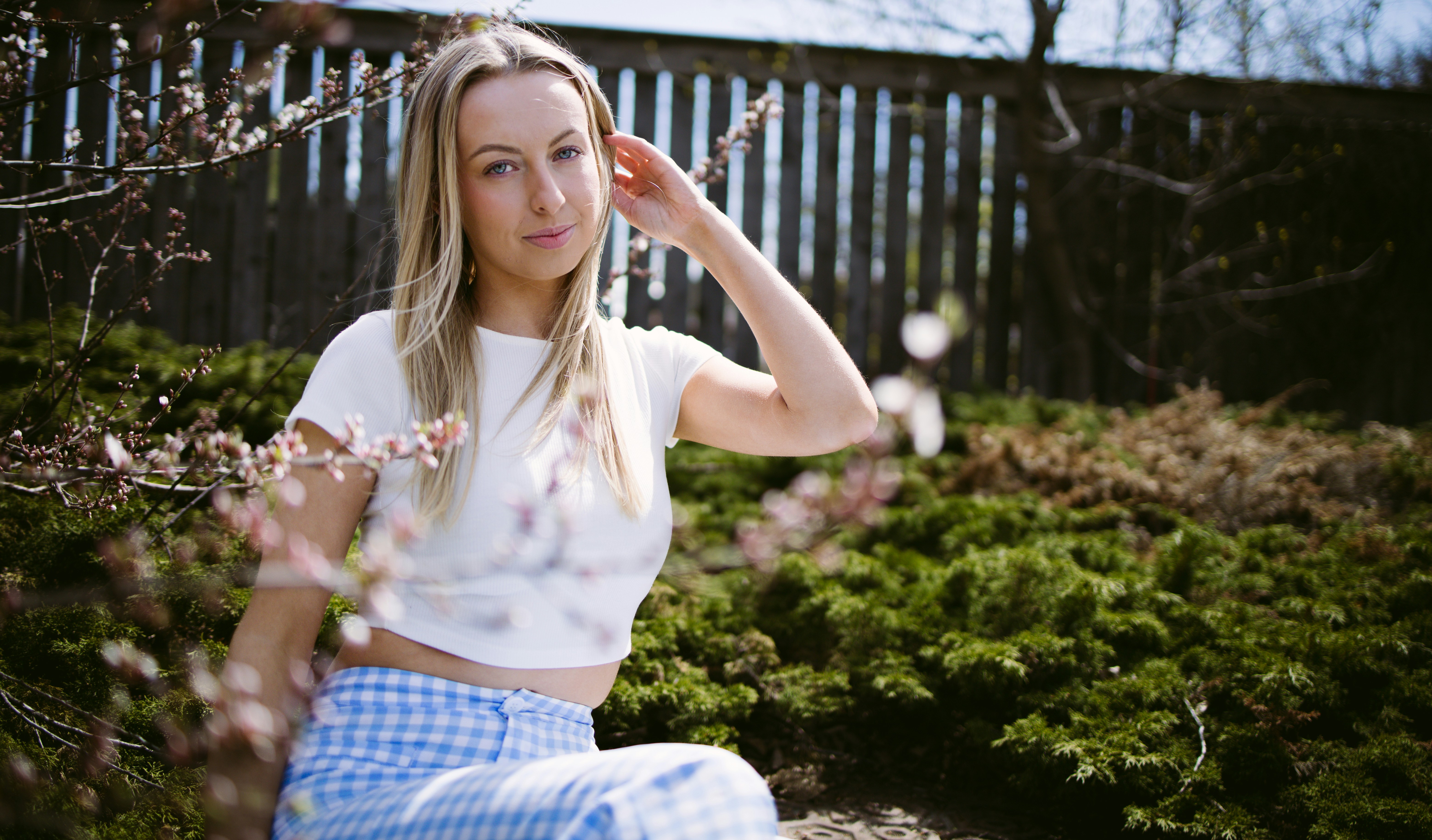 A young woman sits outdoors near blooming trees.