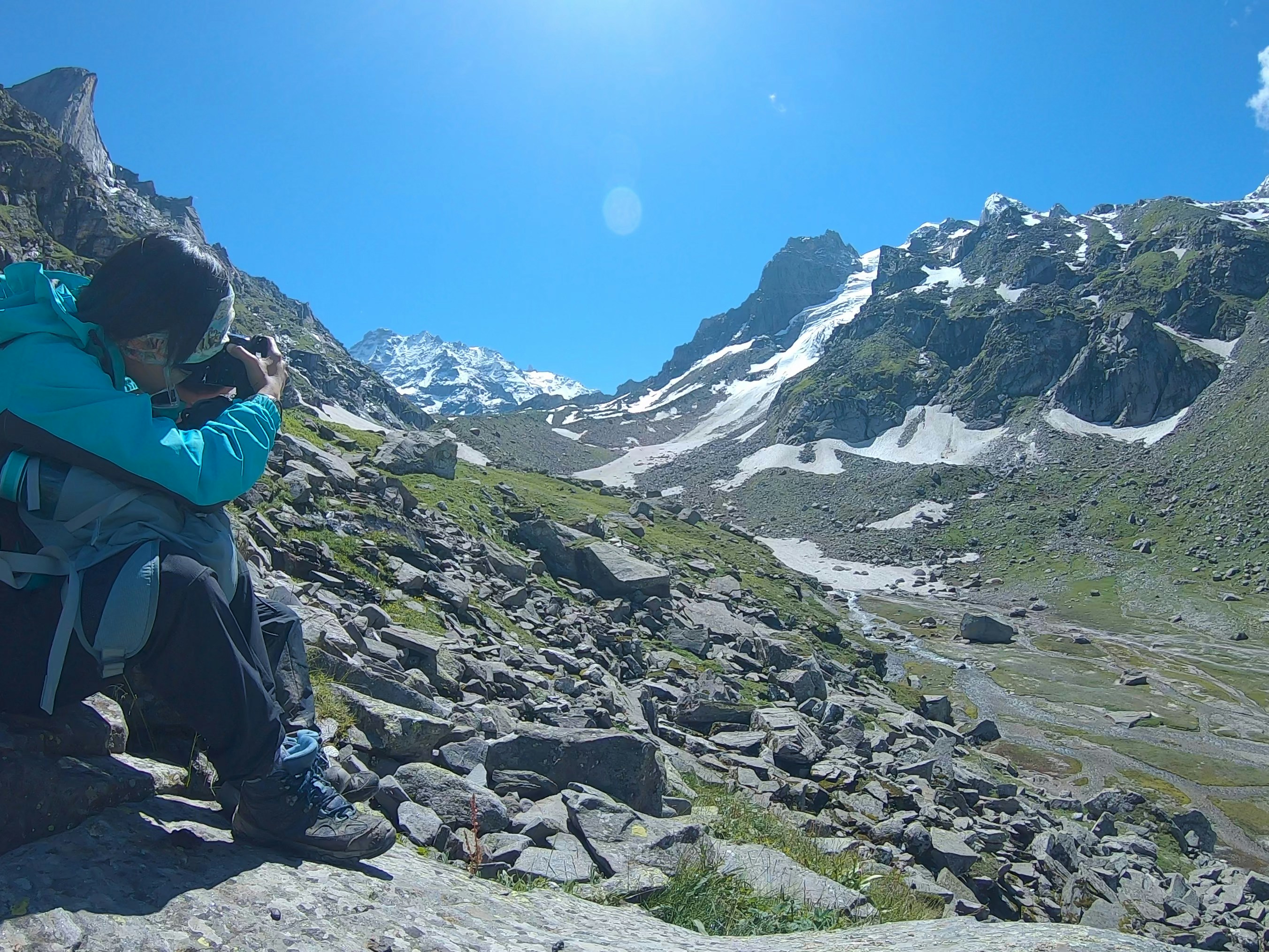 Hiker photographs snowy mountain landscape on sunny day.