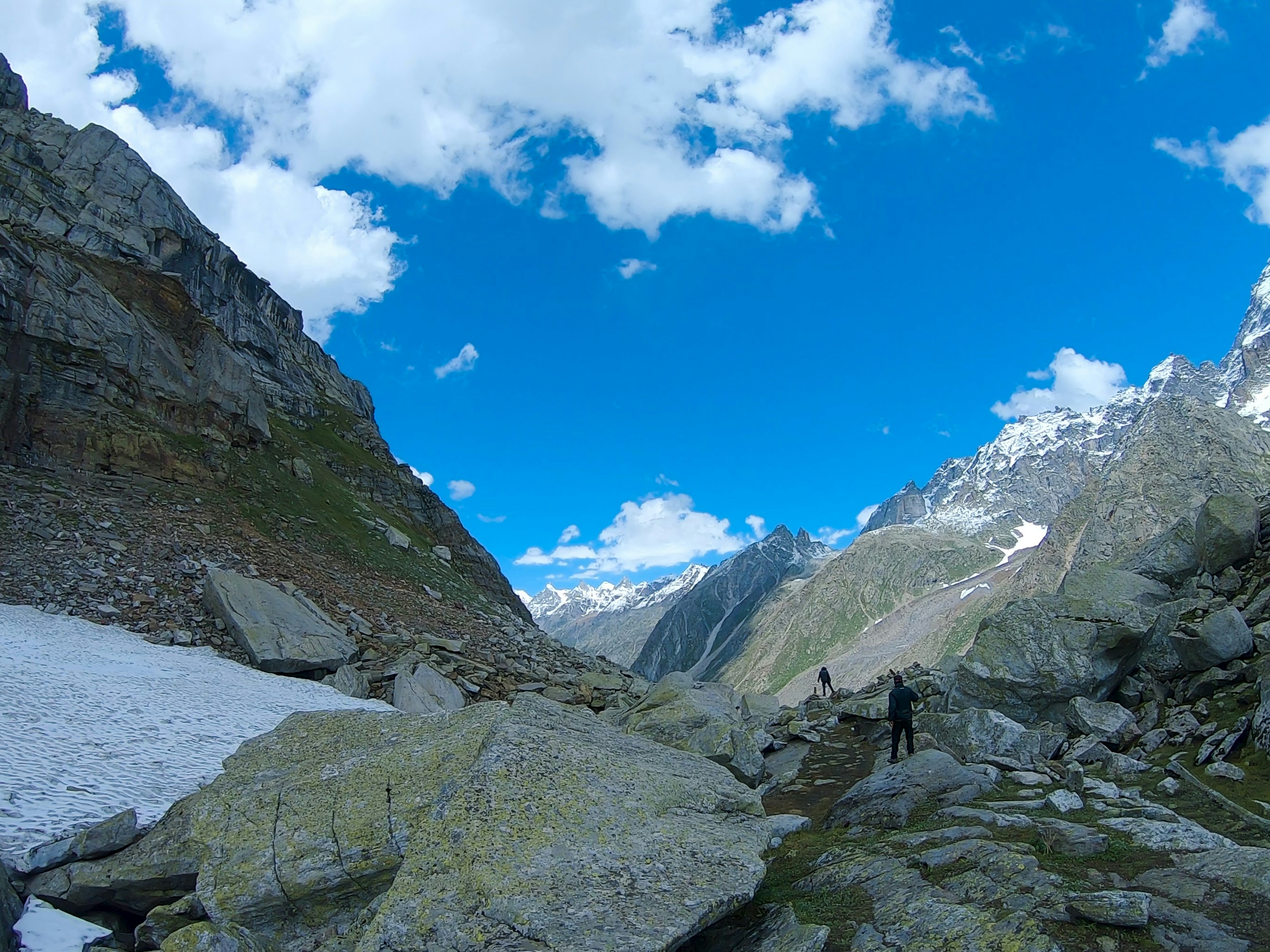 Hikers walk through a rocky mountain pass under blue sky.