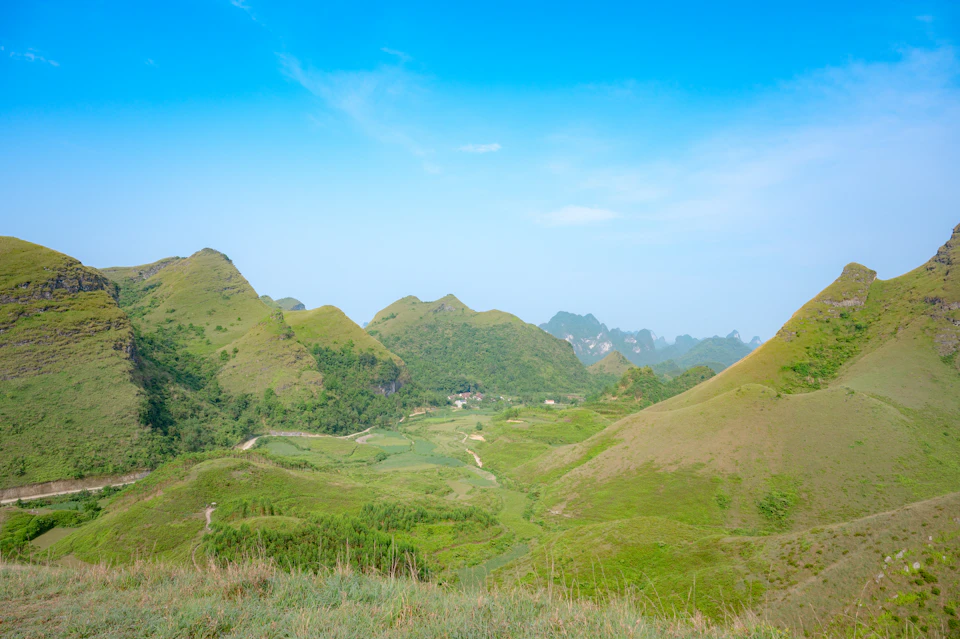 Mountainous landscape with lush green valley between two towering peaks in clear blue sky