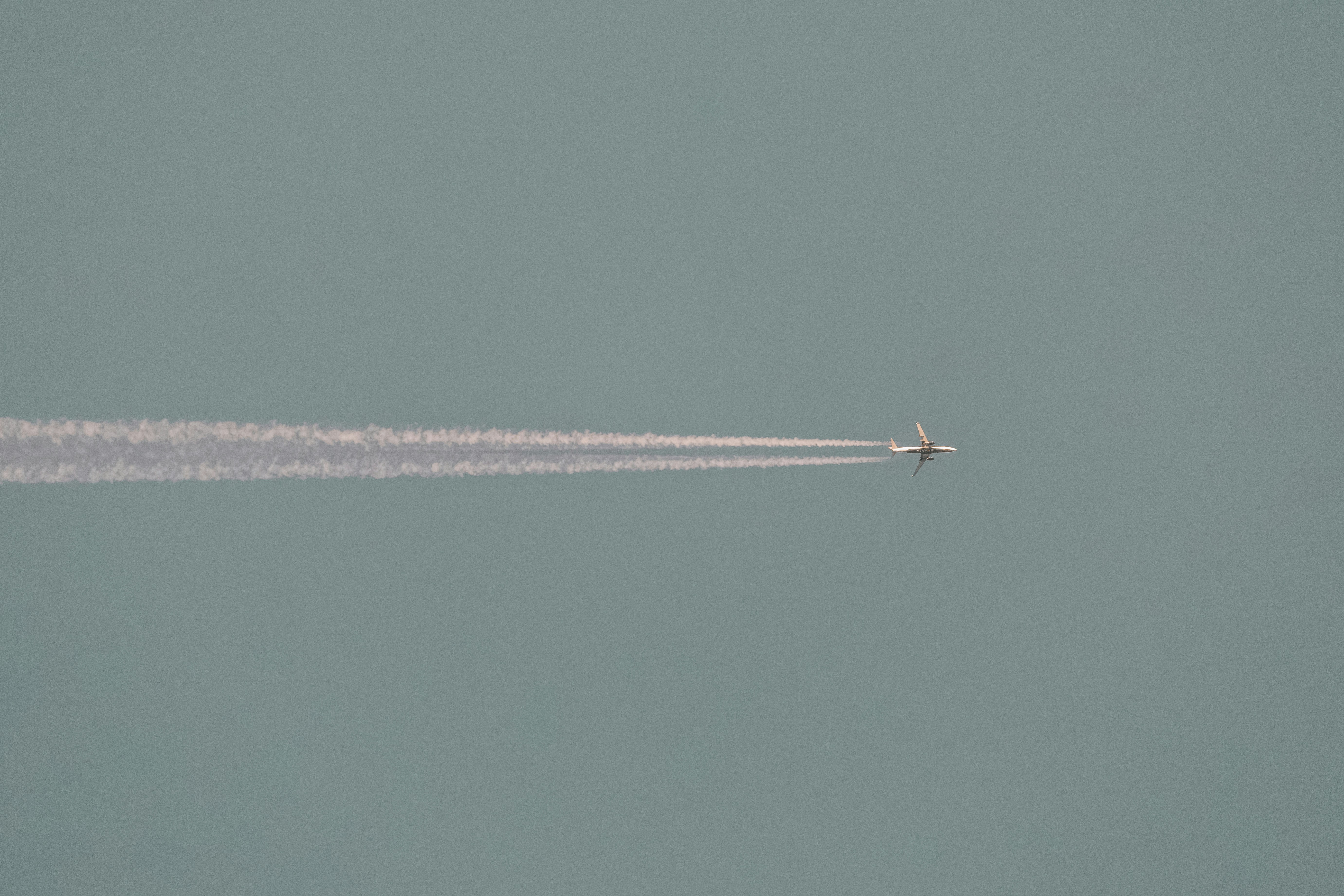 Airplane leaving a white contrail across a pale blue sky.