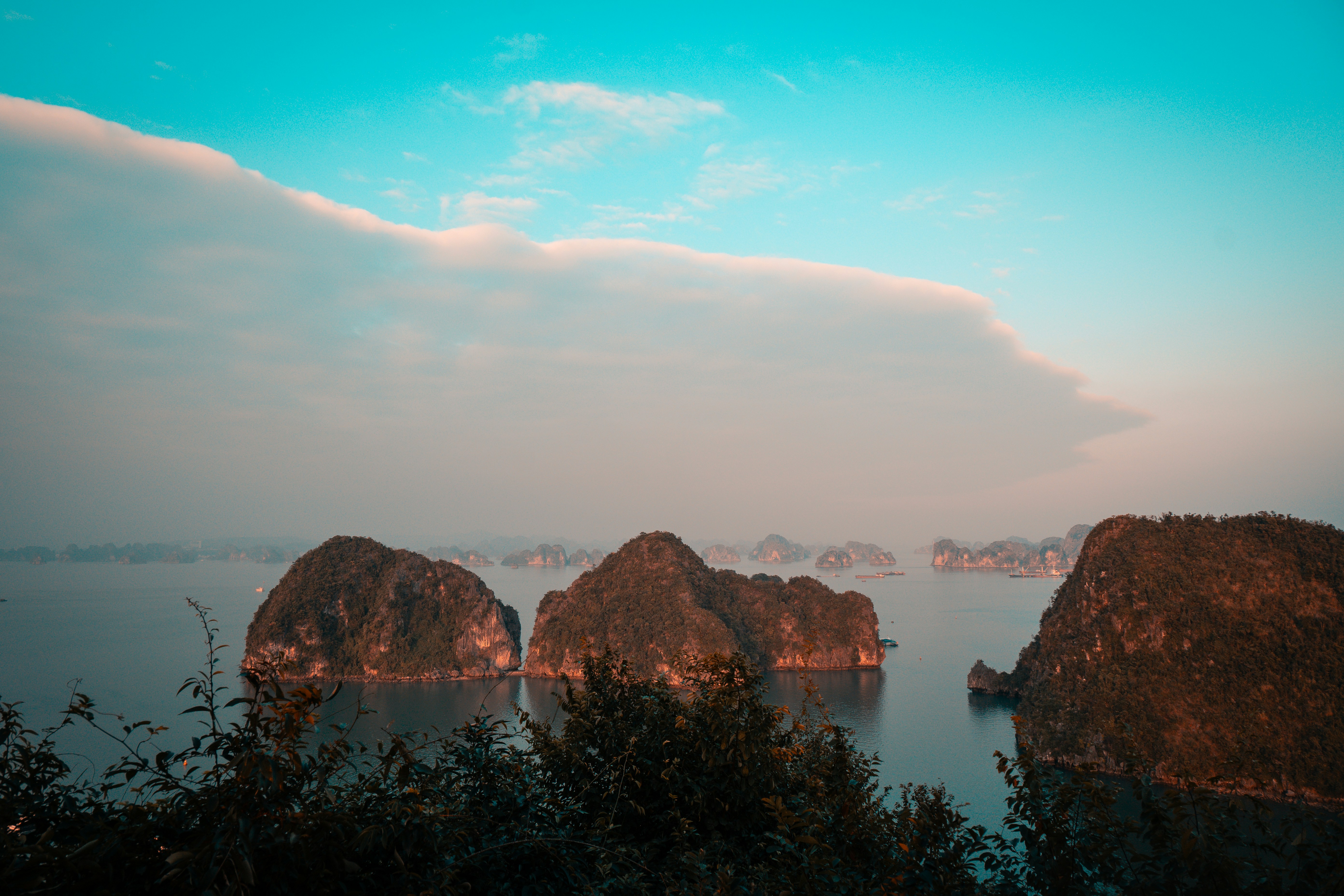 Limestone karsts rise from calm water under a unique cloud.