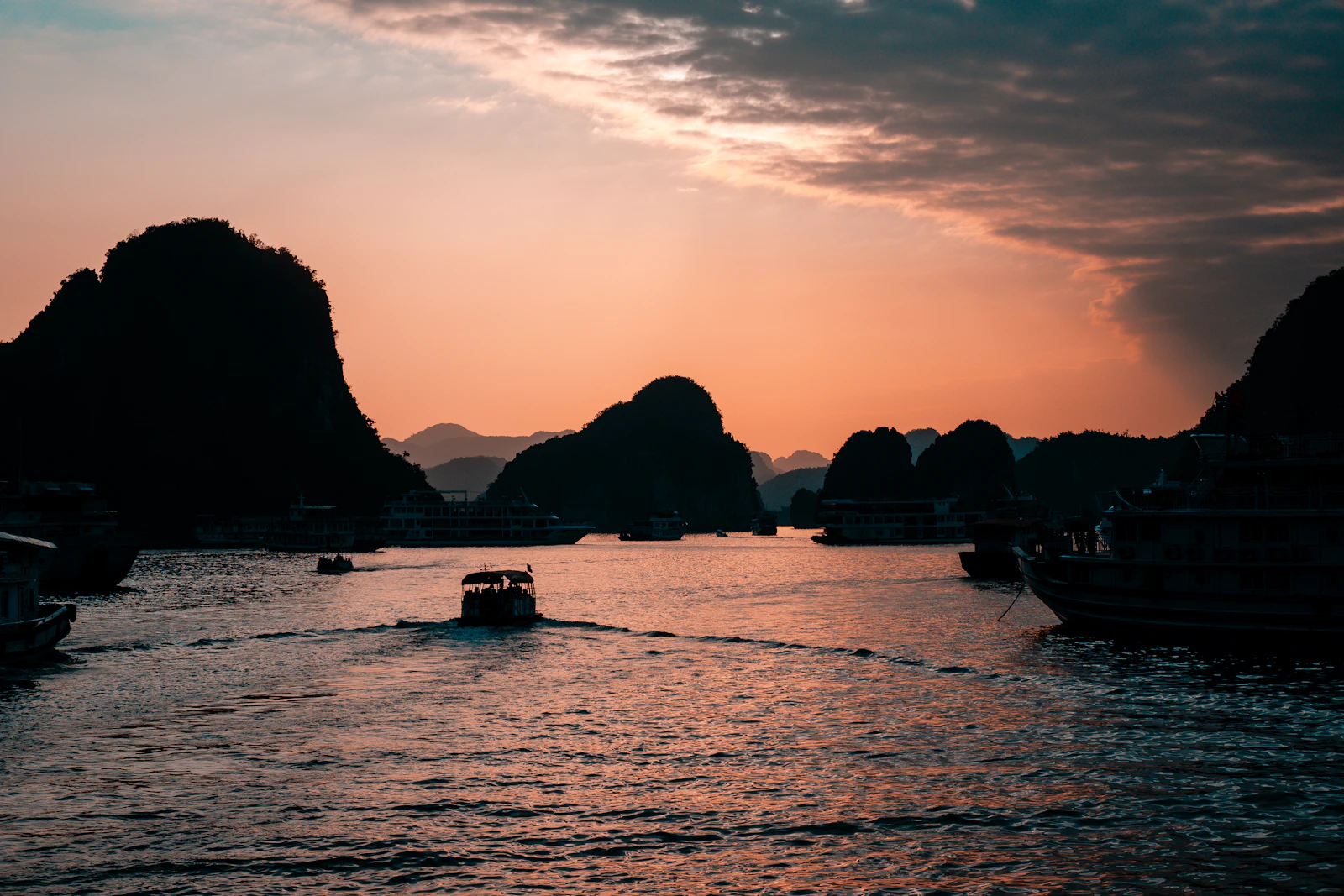 Boats sailing through Ha Long Bay at sunset with limestone mountains in the distance