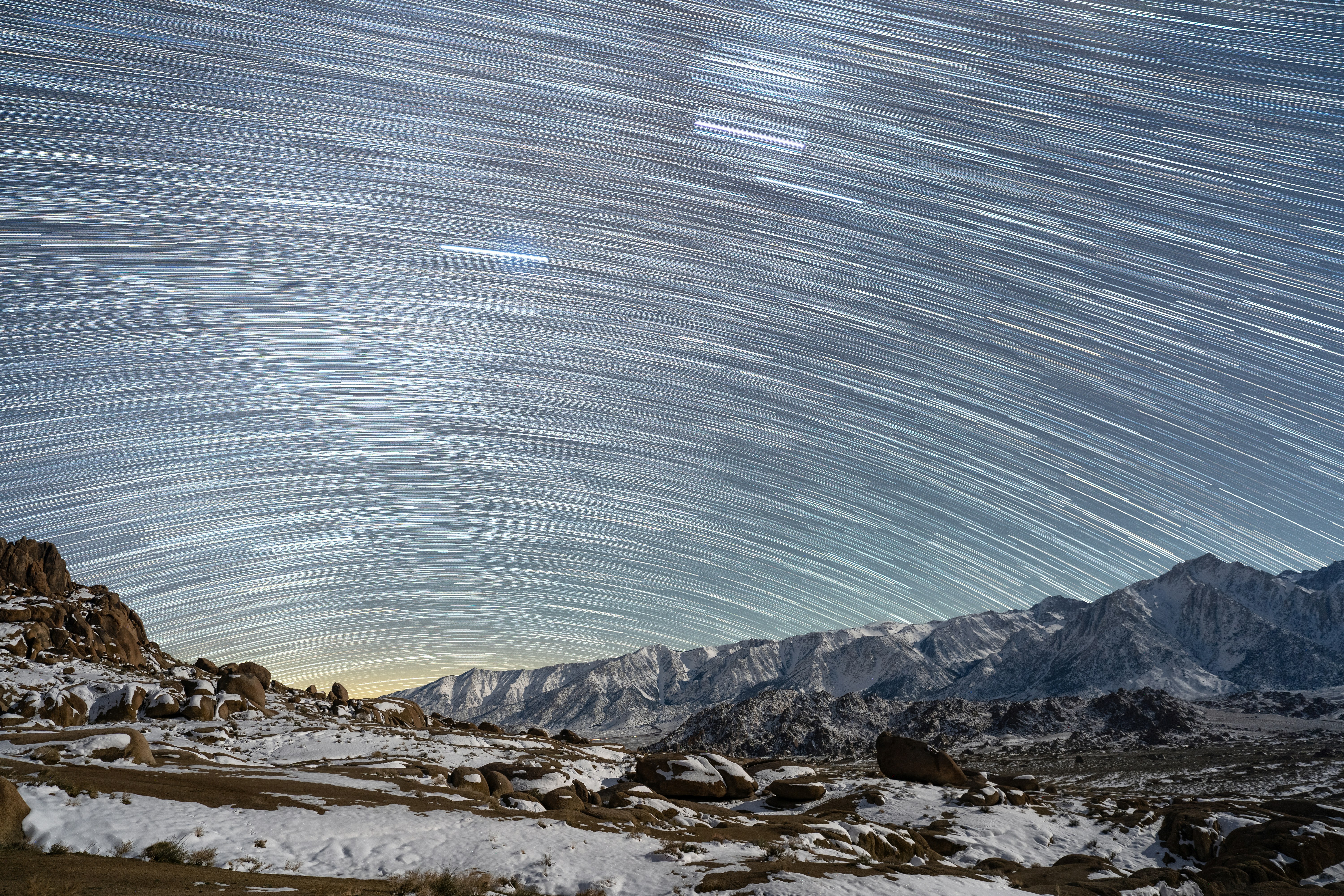 Photo of Star trails over snow-covered mountains at night by Josh Williams