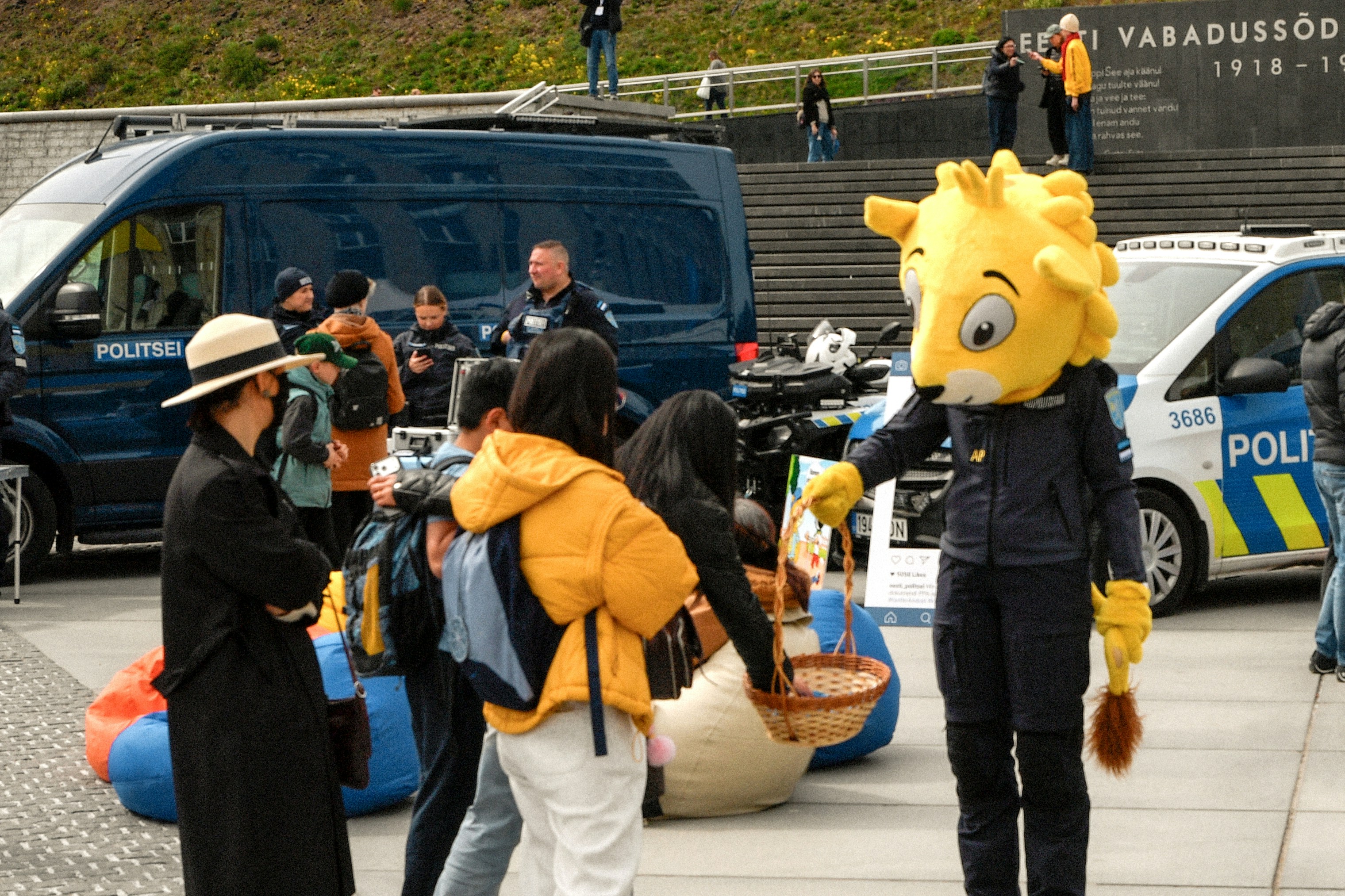La mascotte en uniforme de policier interagit avec les personnes près des voitures de police.