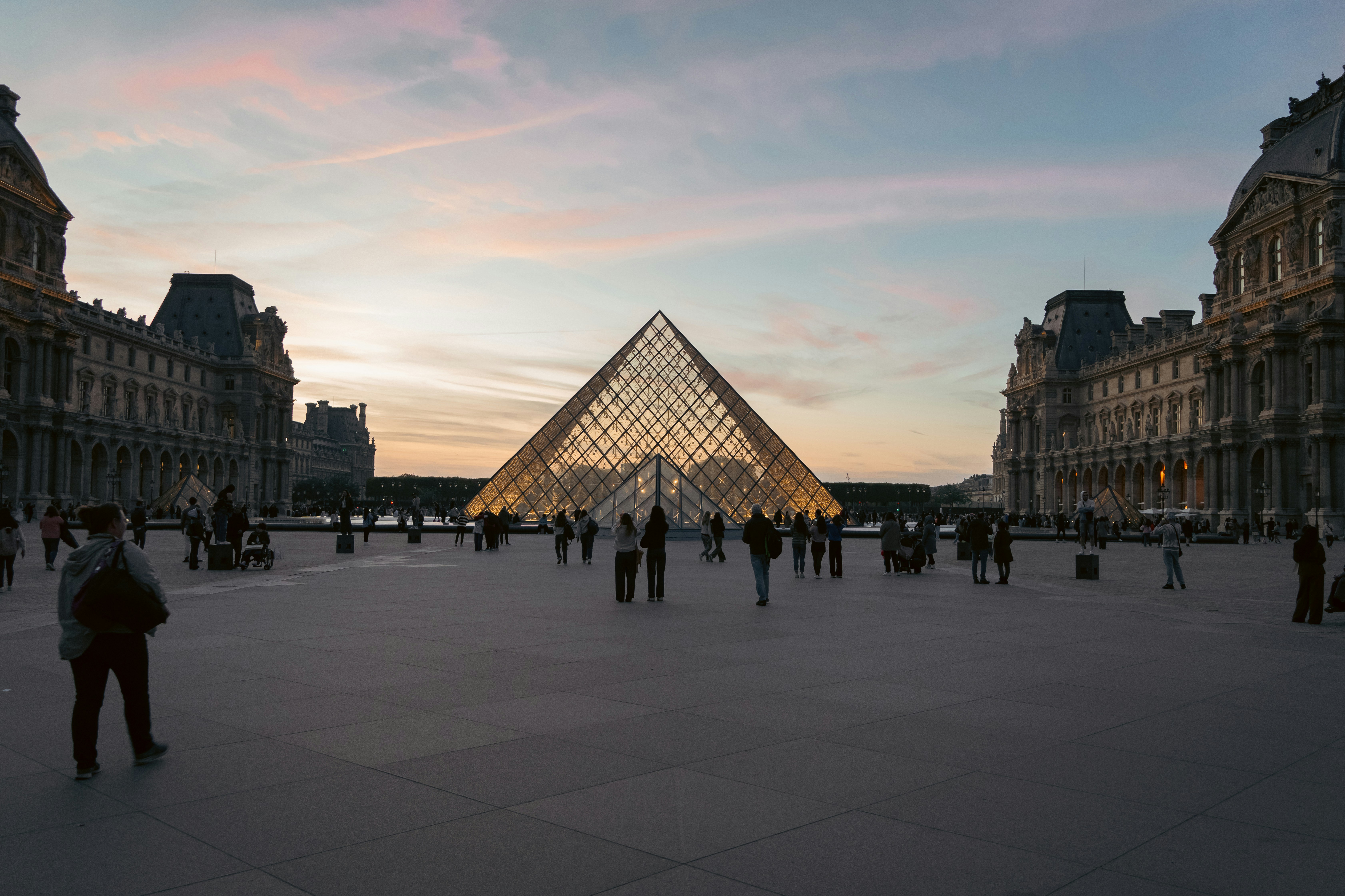 Piramida Louvre saat senja dengan orang-orang berjalan