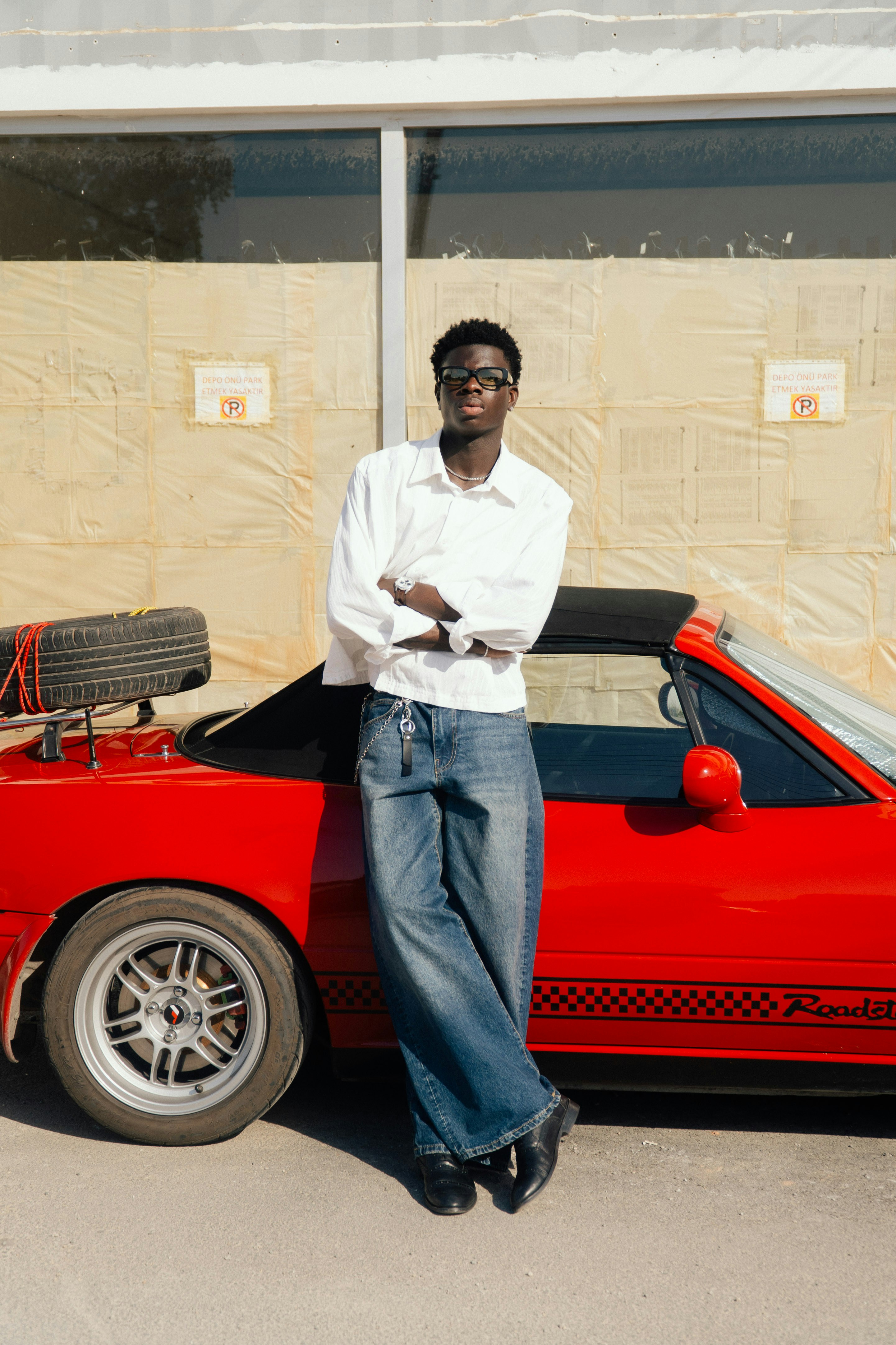 Young man in glasses leaning on red convertible car