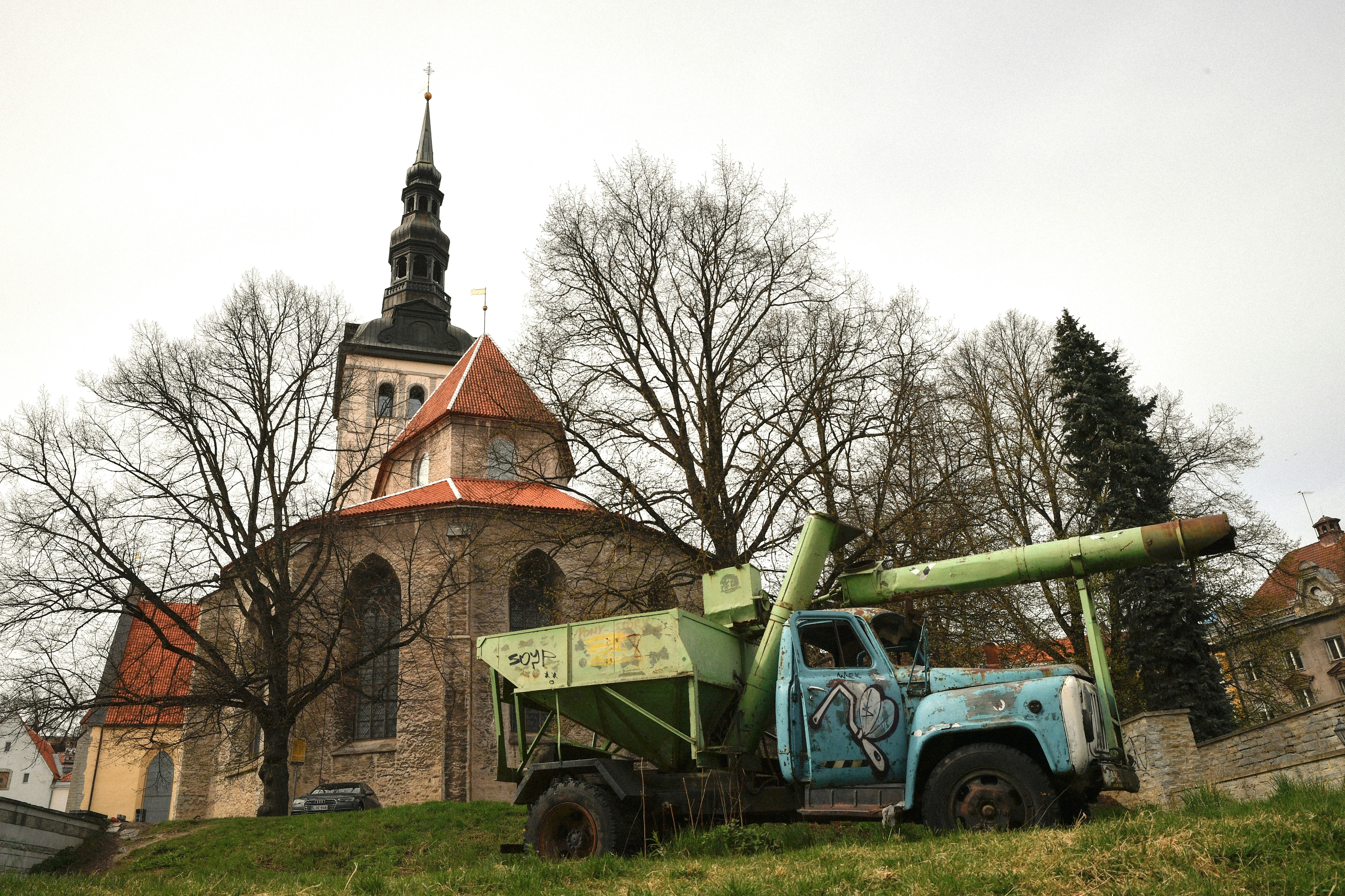 Contrast of Eras: Vintage Soviet Truck and St. Nicholas Church in Tallinn: A striking visual contrast featuring a weathered vintage Soviet-era ZIL truck with graffiti in the foreground and the historic 13th-century St. Nicholas Church (Niguliste) in the background, located in the UNESCO-listed Tallinn Old Town, Estonia.