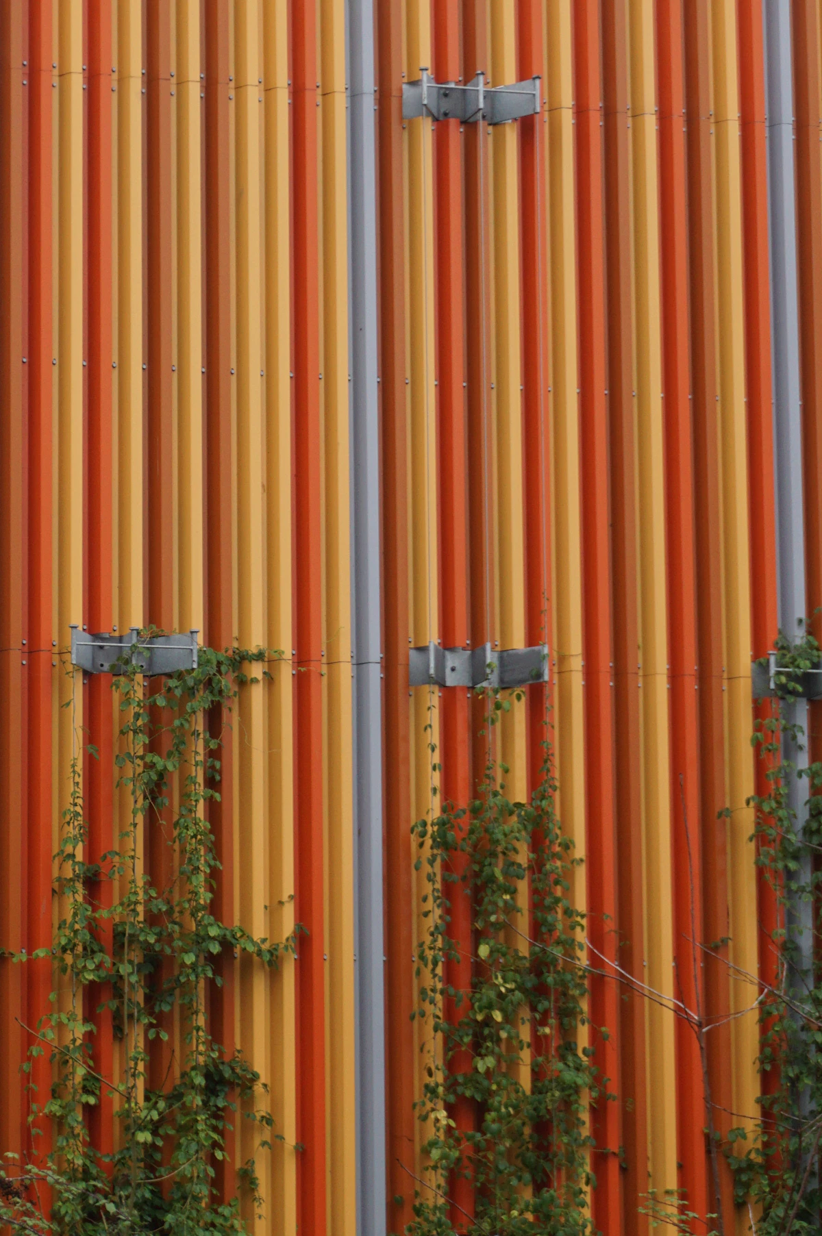 Lodret profilbeklædning i orange og gule nuancer på en bygningsfacade