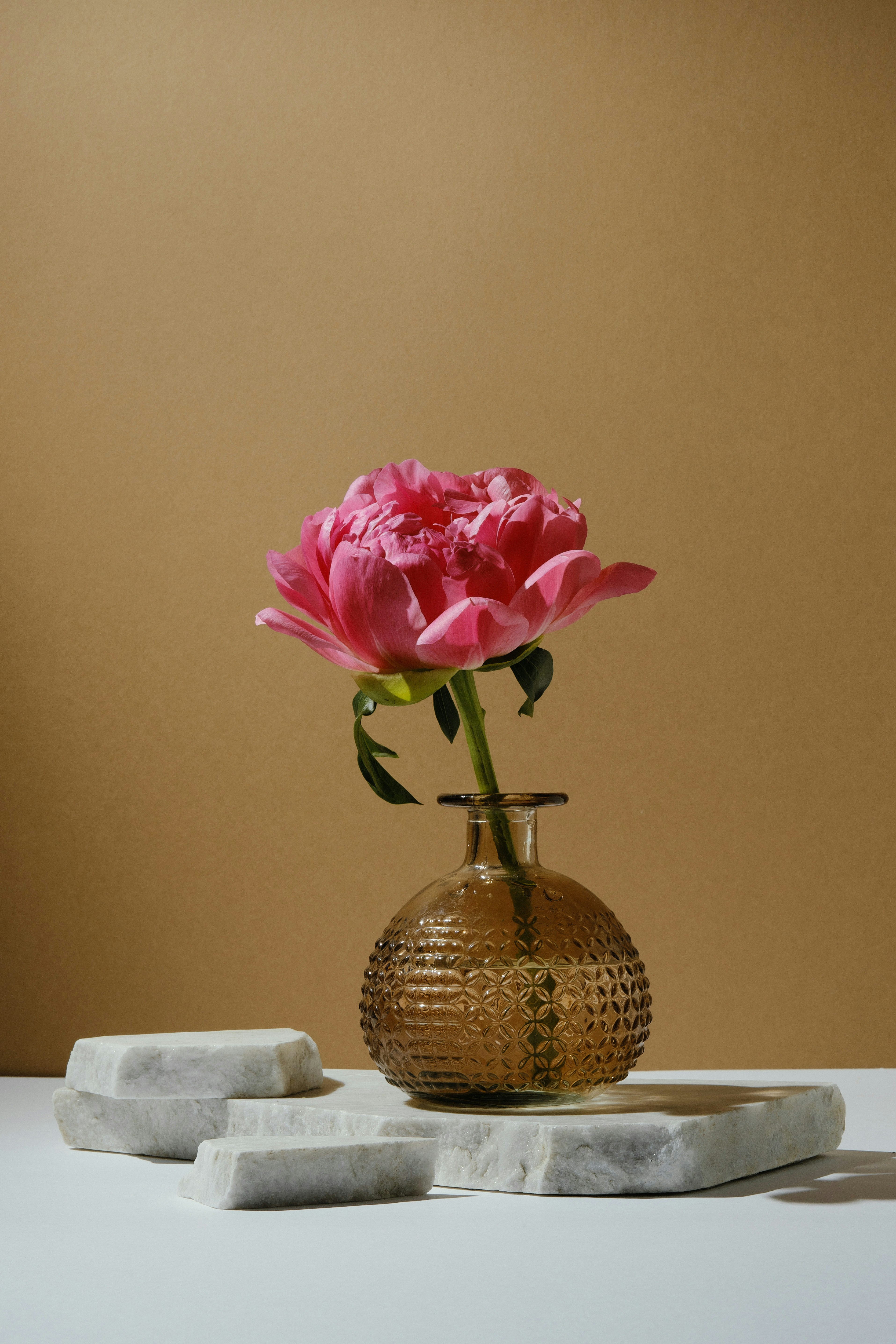Pink peony in a textured glass vase on marble