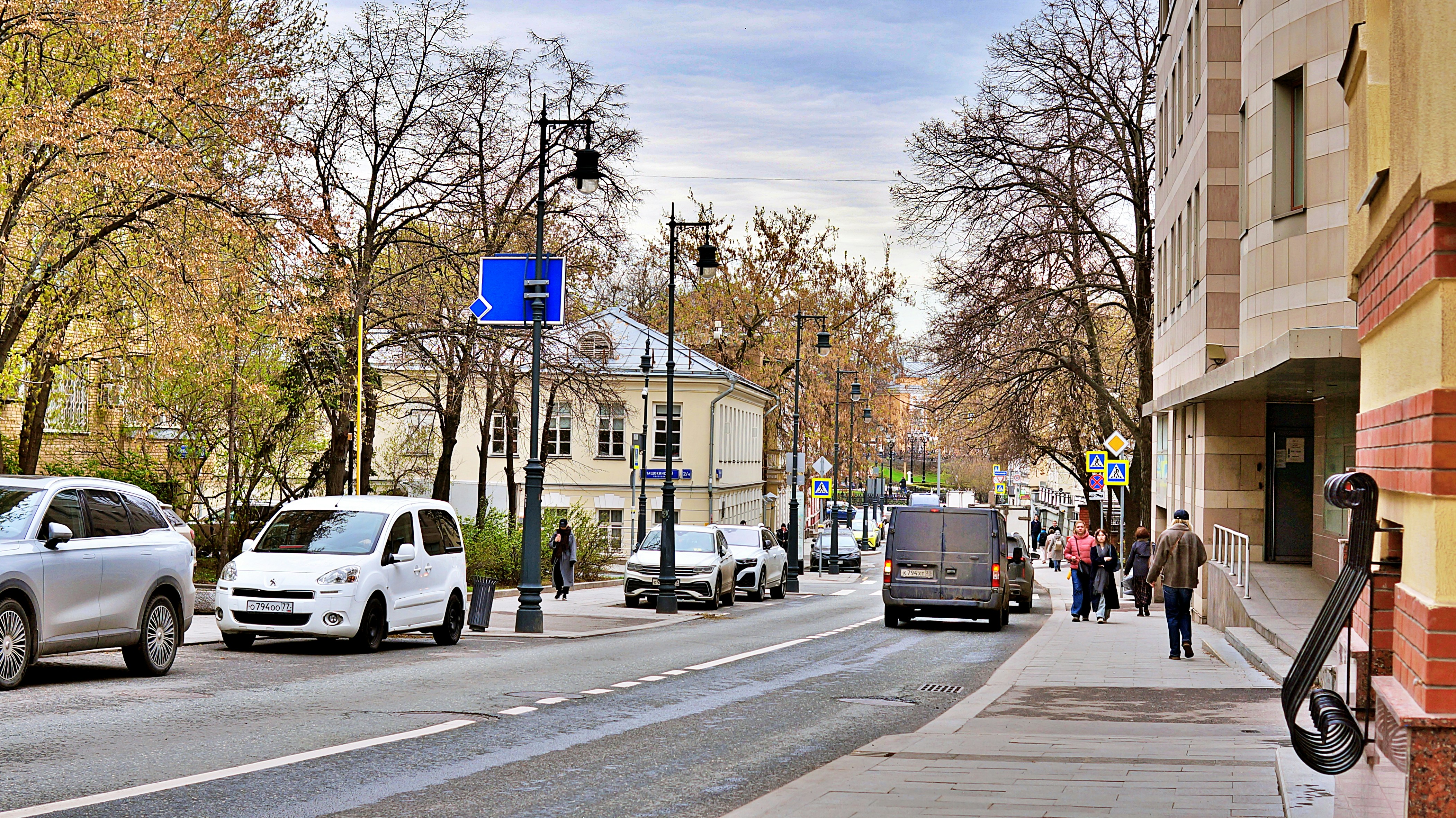 Cars drive down a tree-lined city street.