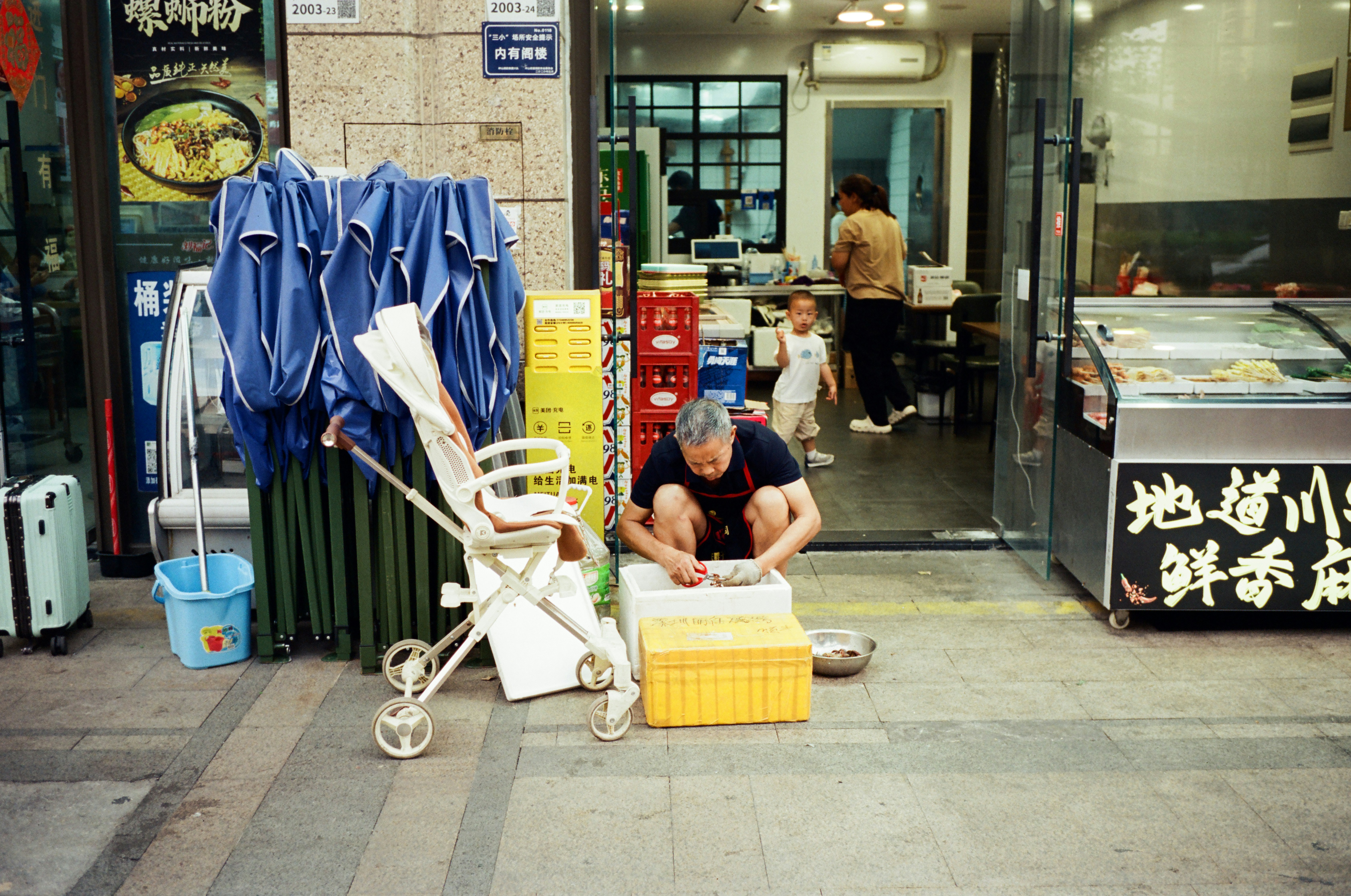 Elderly person sitting on street next to stroller.