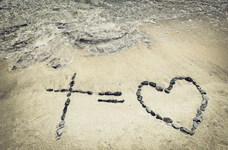 Cross equals heart made of stones on sand