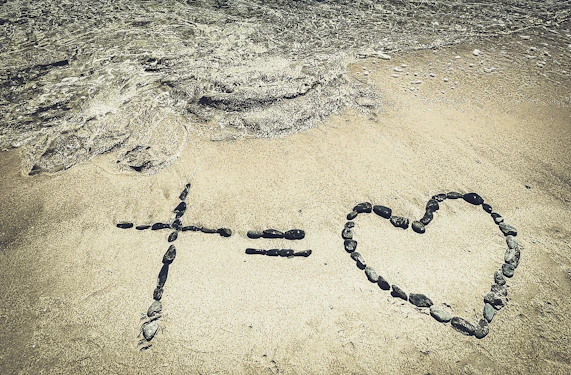 Cross equals heart made of stones on sand