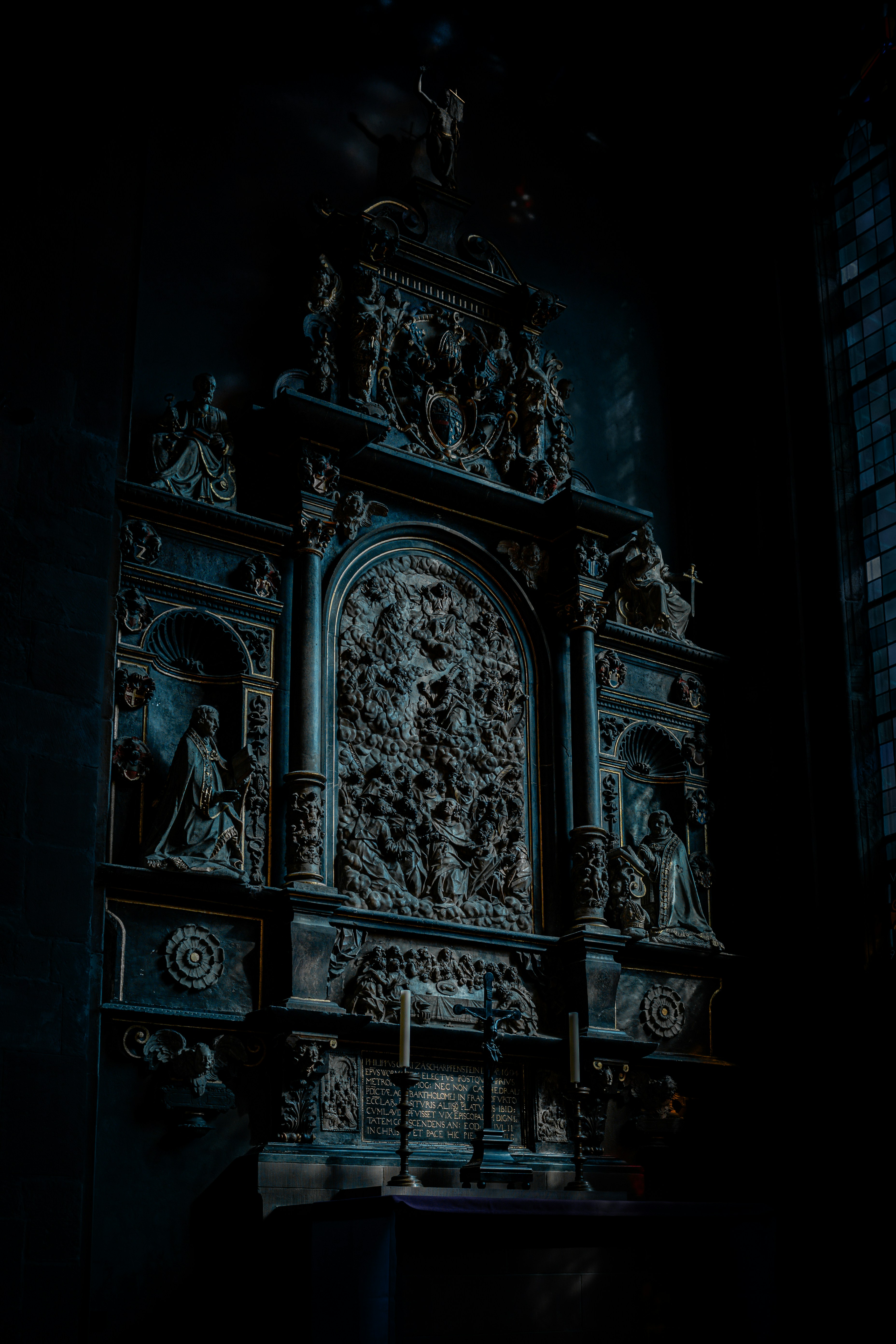 Ornate dark relief sculpture with candles below