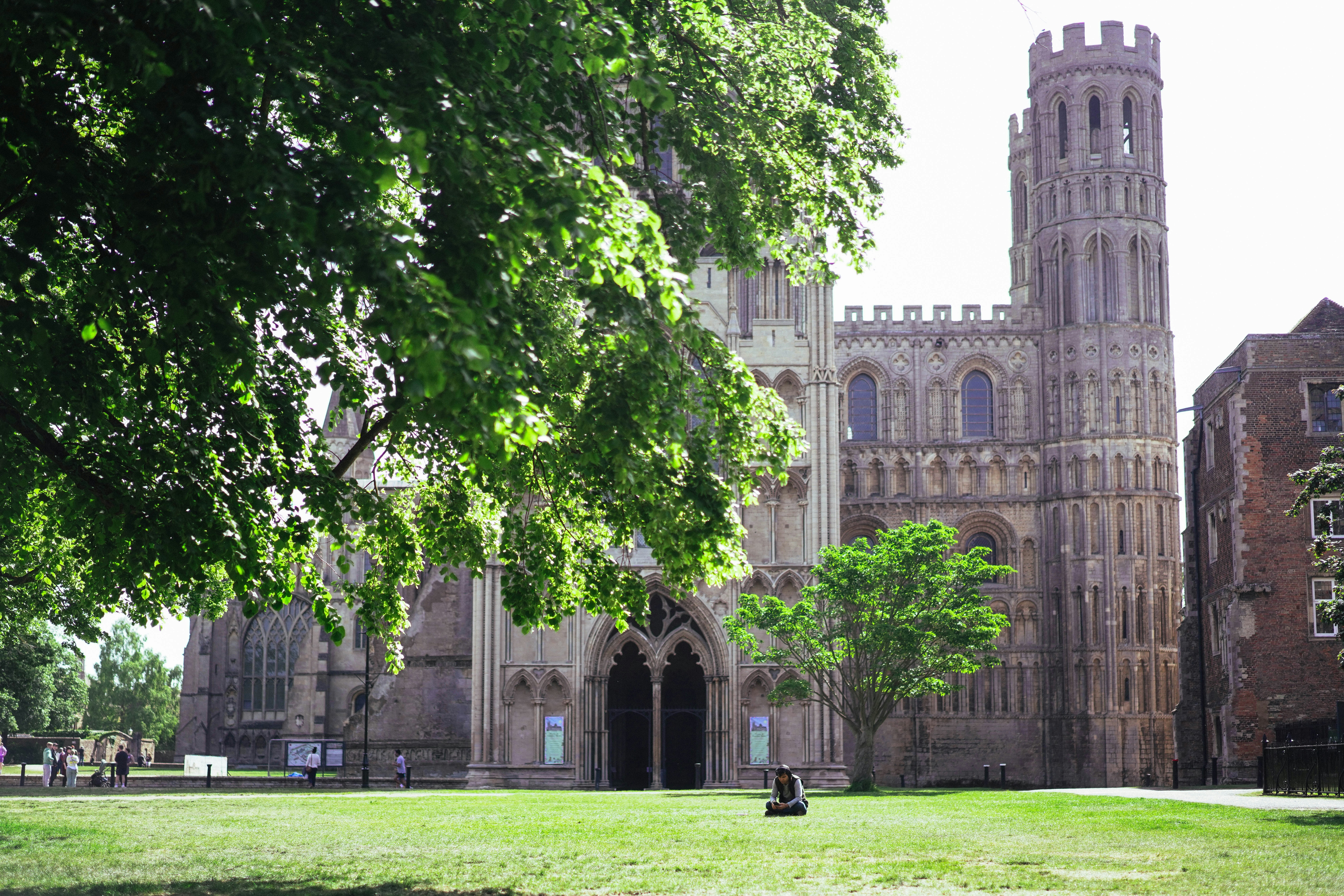 Large stone cathedral with a tower and green lawn.